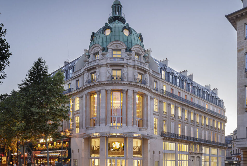 Façade d'un bâtiment haussmannien avec une coupole verte distincte et de grandes fenêtres illuminées. Architecture élégante située au cœur d'un quartier animé, mettant en valeur le logo Pathé à l'entrée