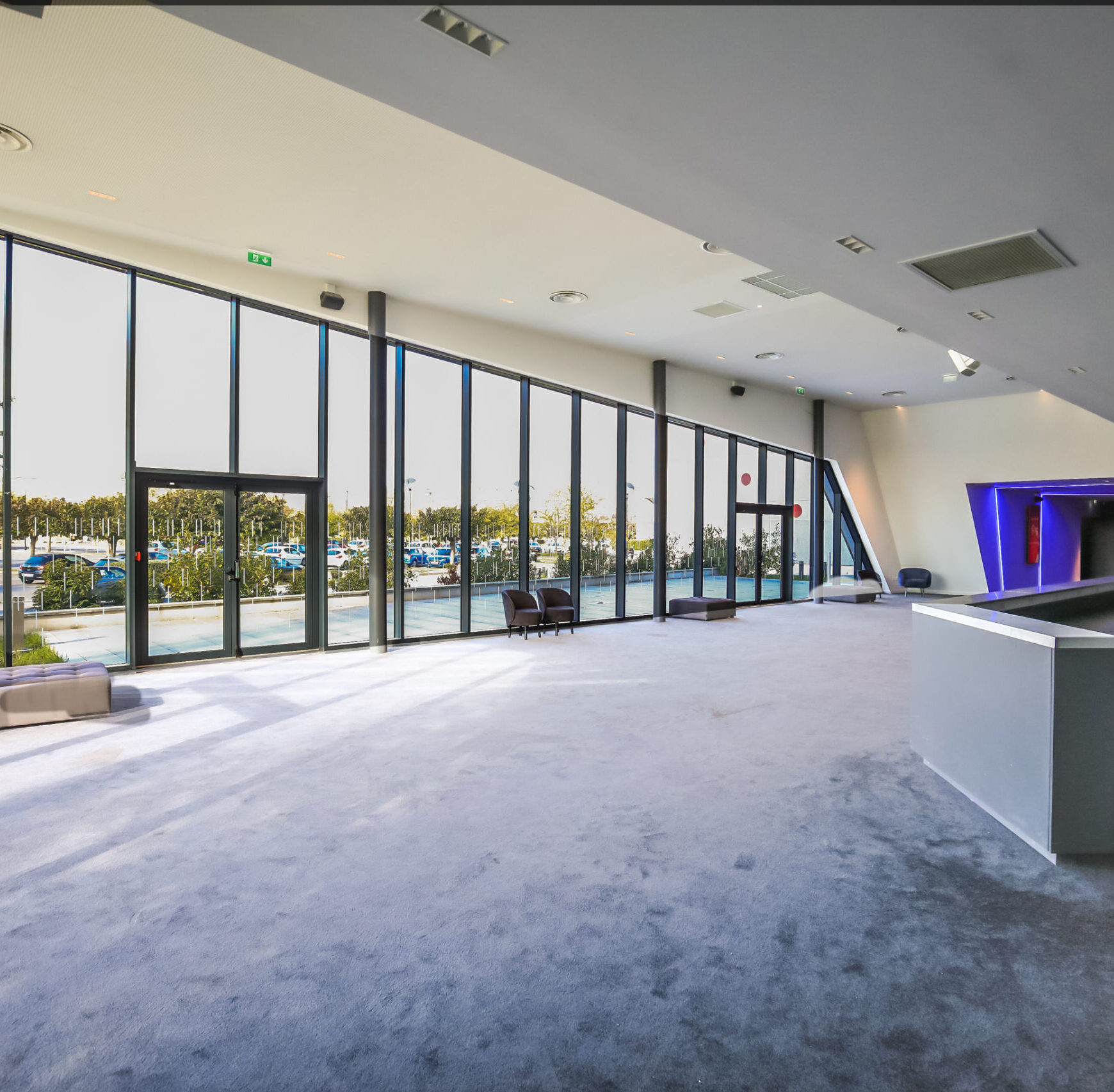 Espace cocktail du cinéma à la lumière du jour grâce à ses grandes baies vitrées, équipé d'un mobilier de réception dans les tons bleu et gris.