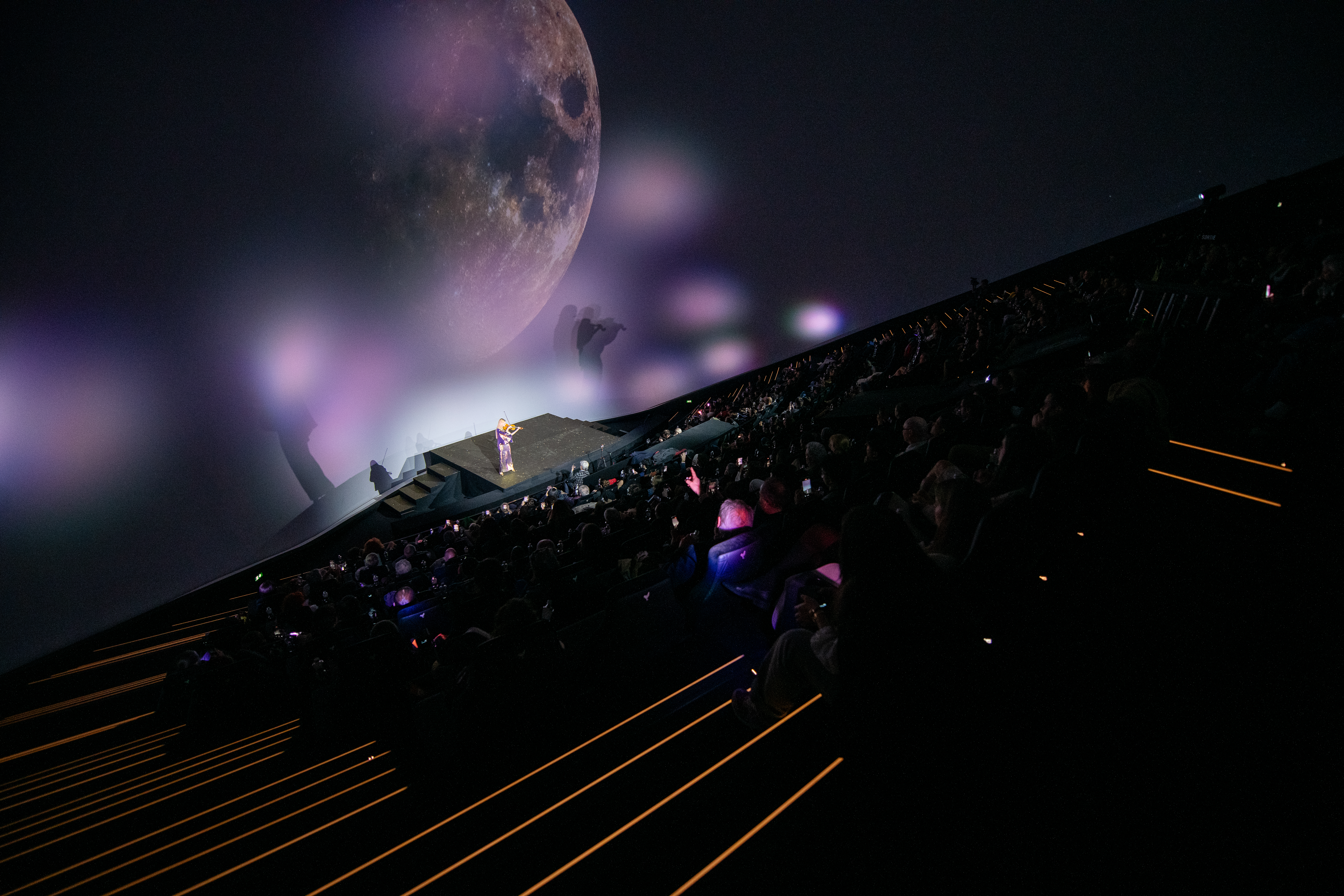 Auditorium du cinéma Pathé La Géode, public présent, violoniste sur scène, éclairage aux tons violets.