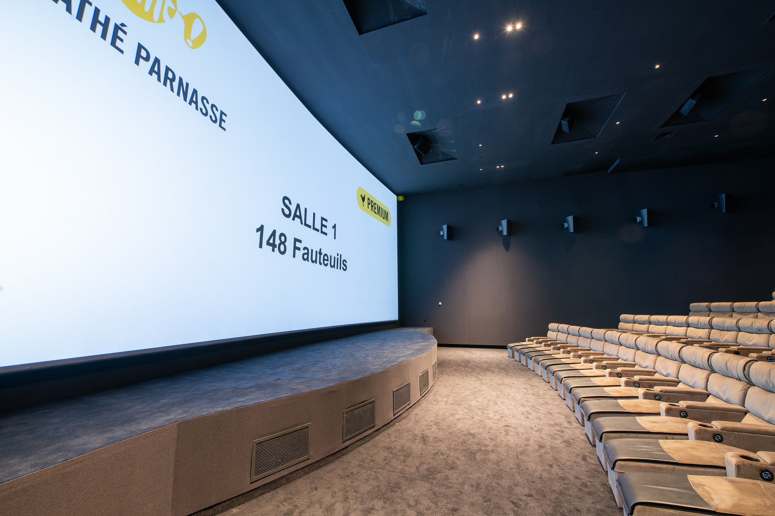 Salle de cinéma Premium avec 148 fauteuils inclinables et écran XXL, ambiance sombre et moderne.