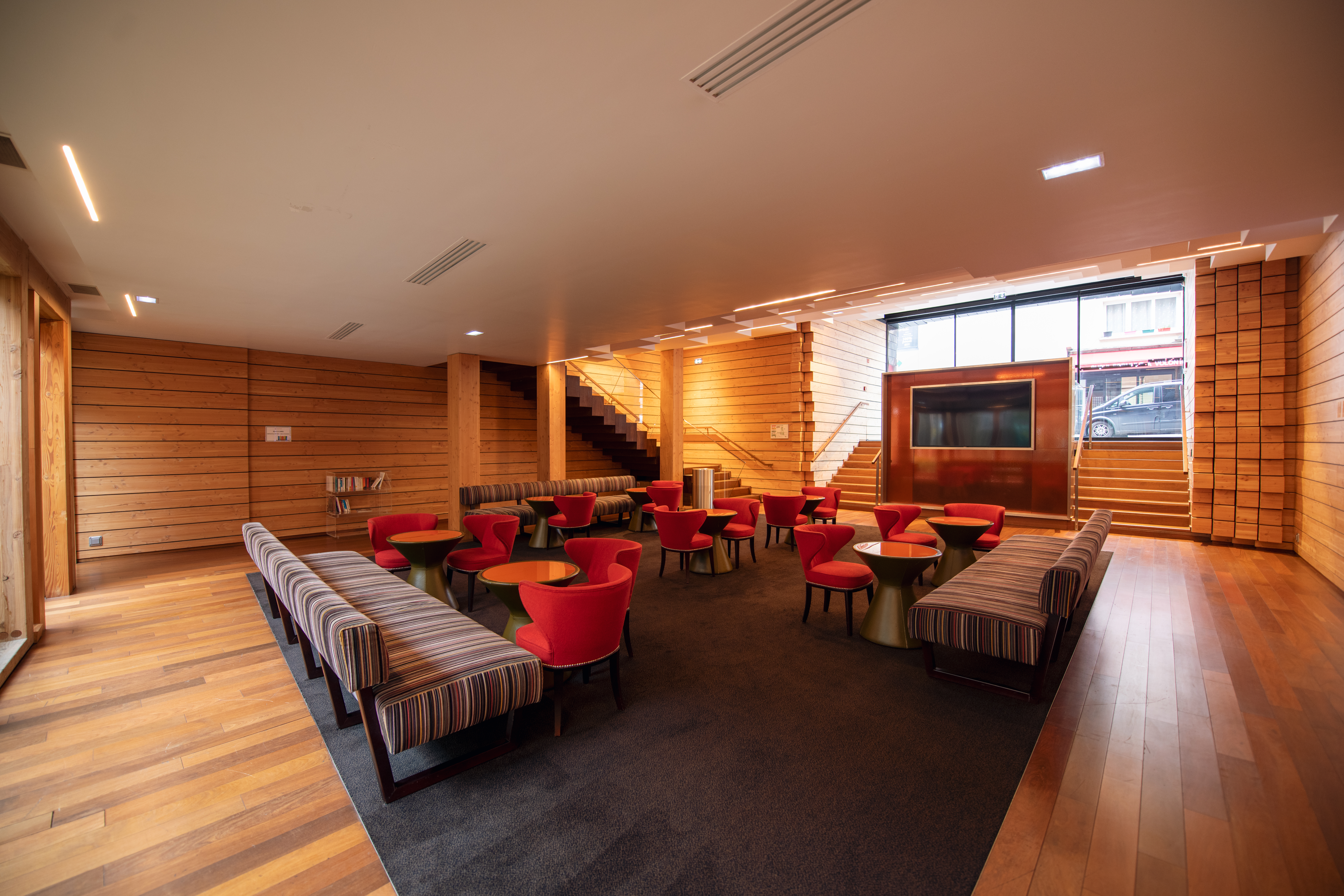 Espace cocktail du cinéma, équipé de tables, chaises et canapés, idéal pour des moments conviviaux et des réceptions dans un cadre chaleureux en bois.