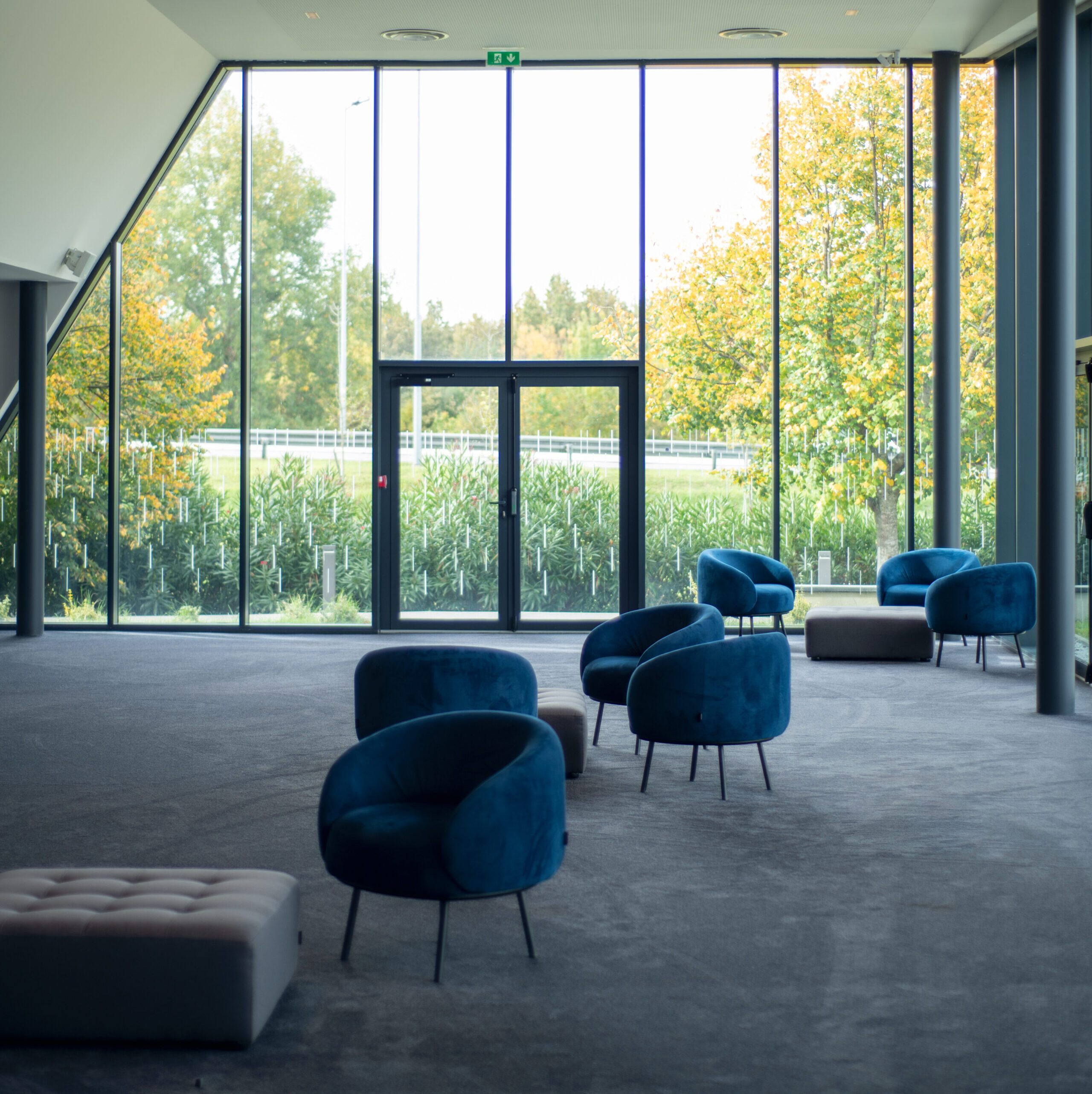 Espace cocktail du cinéma à la lumière du jour grâce à ses grandes baies vitrées, équipé d'un mobilier de réception dans les tons bleu et gris.