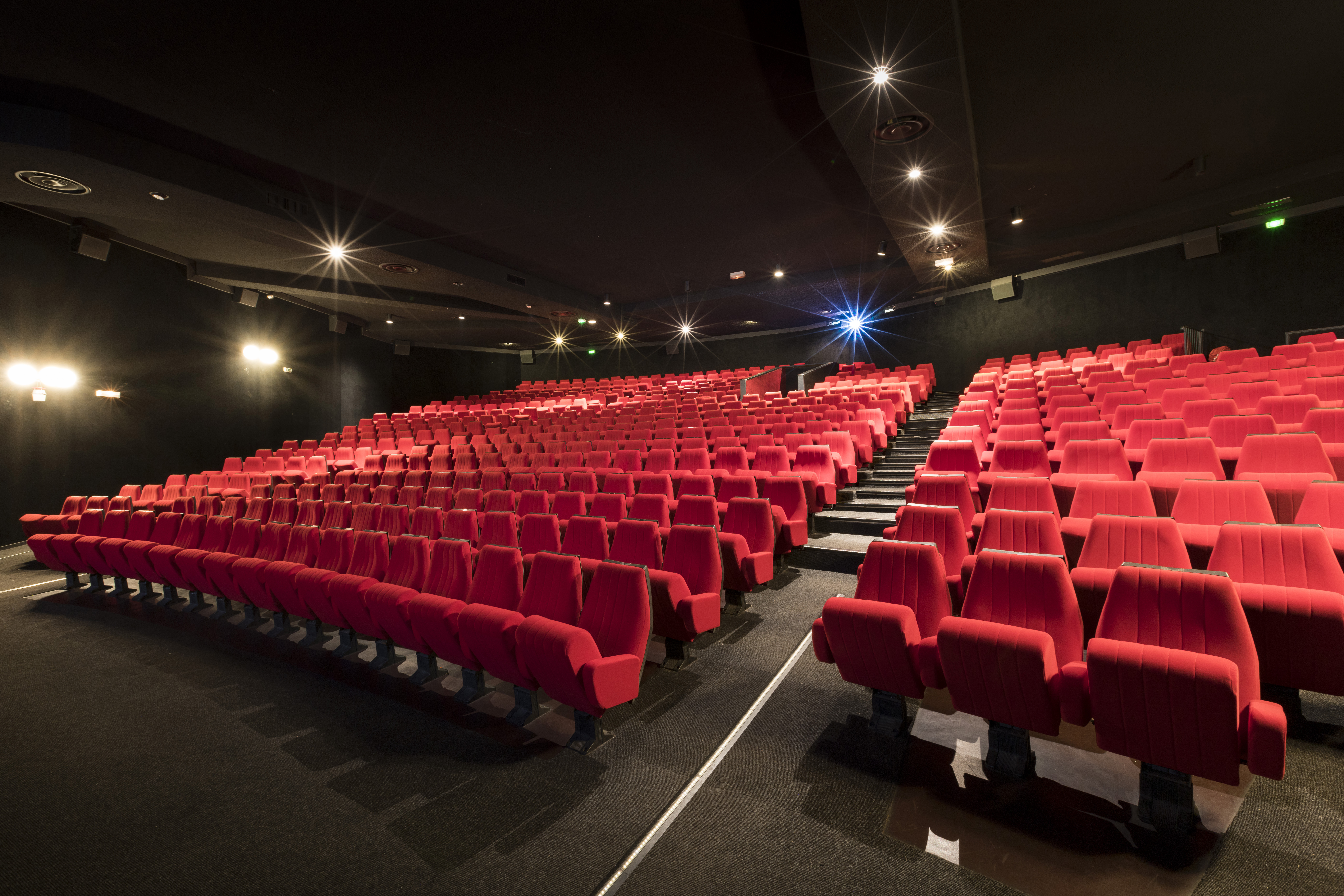 Vue latérale de la salle de cinéma montrant les fauteuils en velours rouges et l’agencement des rangées ainsi que son espace scénique.