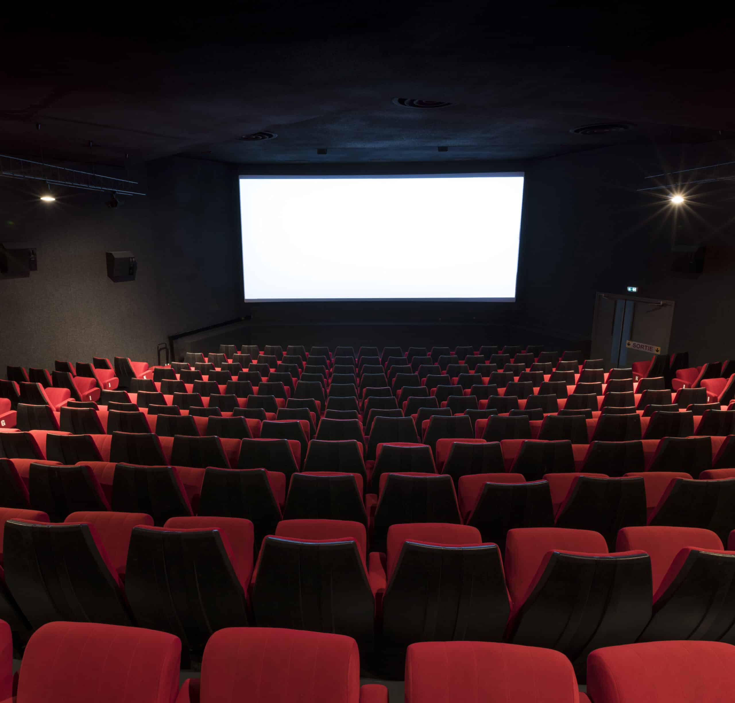 Vue depuis l’arrière d'une salle de cinéma avec ses rangées de fauteuils en velours rouges orientés vers l’écran.