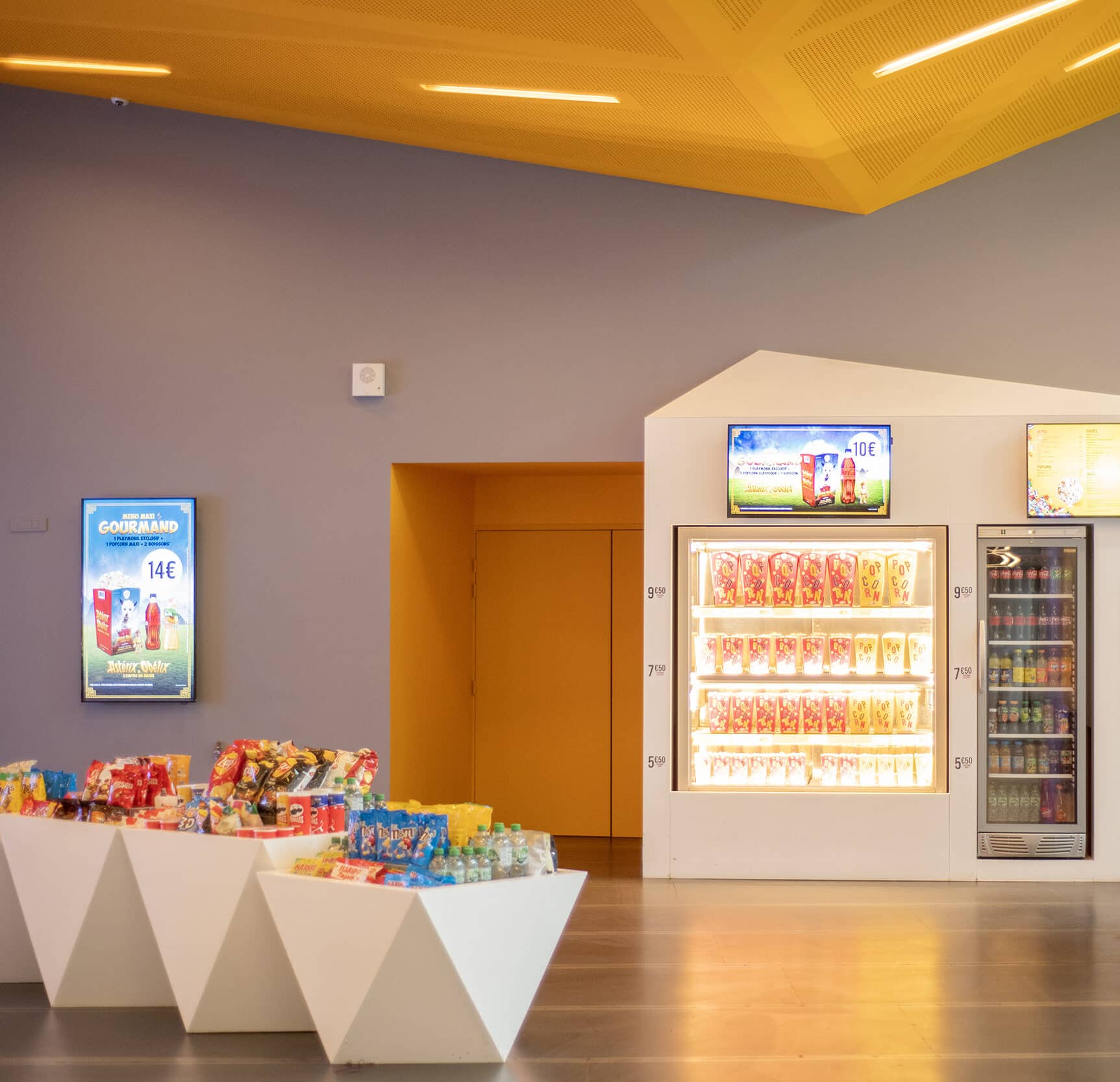 Espace confiserie du cinéma Pathé avec comptoir de pop-corn, distributeurs de boissons en libre-service et îlots de snacks et confiseries.