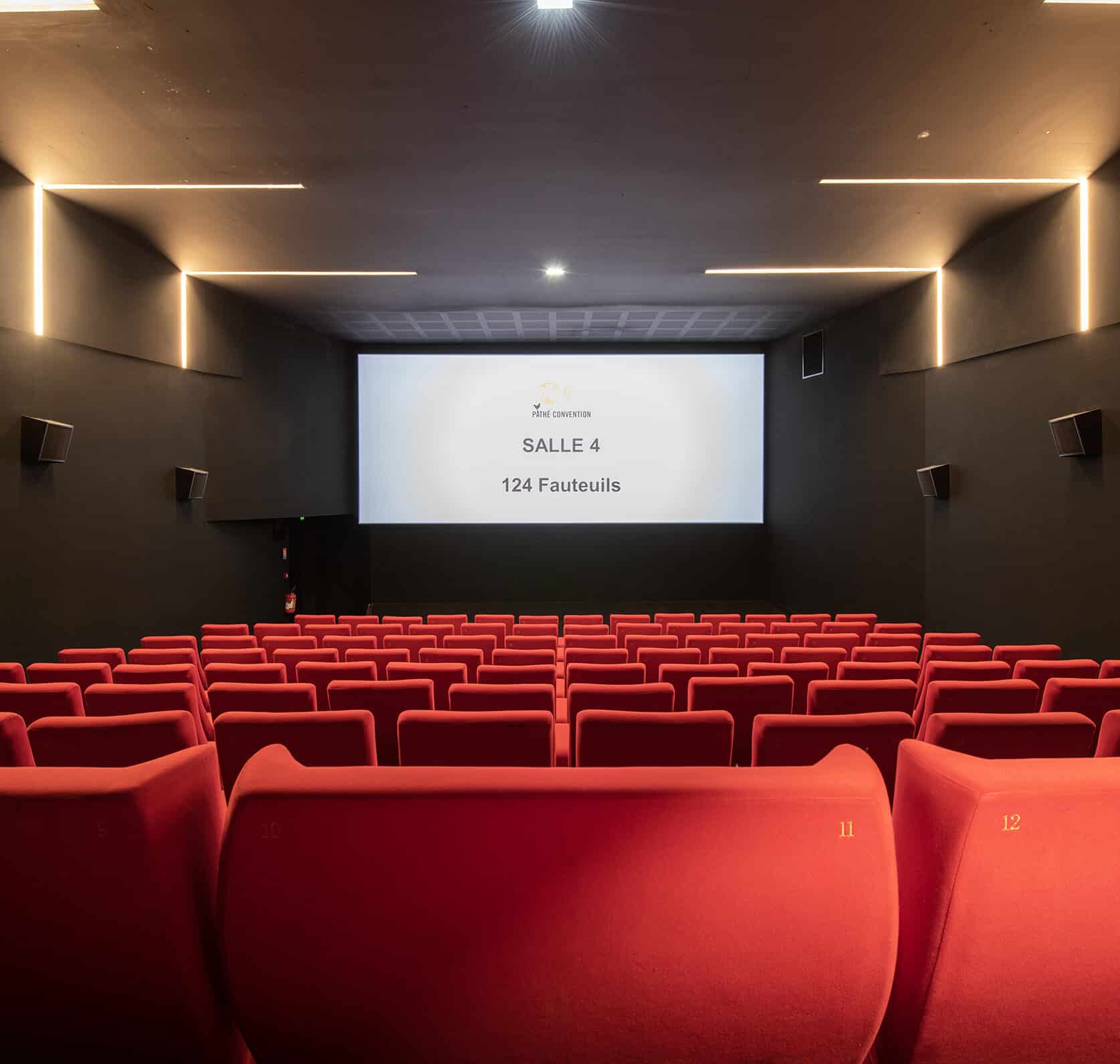 Vue depuis l’arrière de la salle 4 du cinéma Pathé Convention avec rangées de fauteuils en velours rouges orientés vers l’écran.