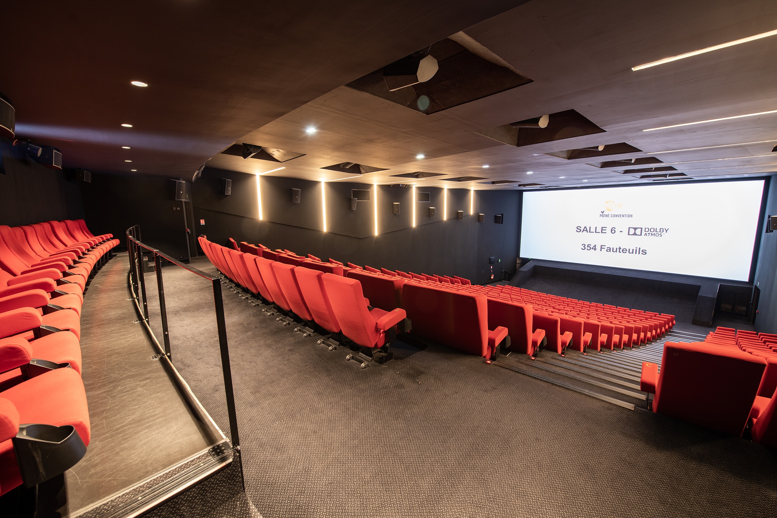 Vue depuis l’arrière de la salle 6 équipée de la technologie Dolby Atmos du cinéma Pathé Convention avec rangées de fauteuils en velours rouges orientés vers l’écran.