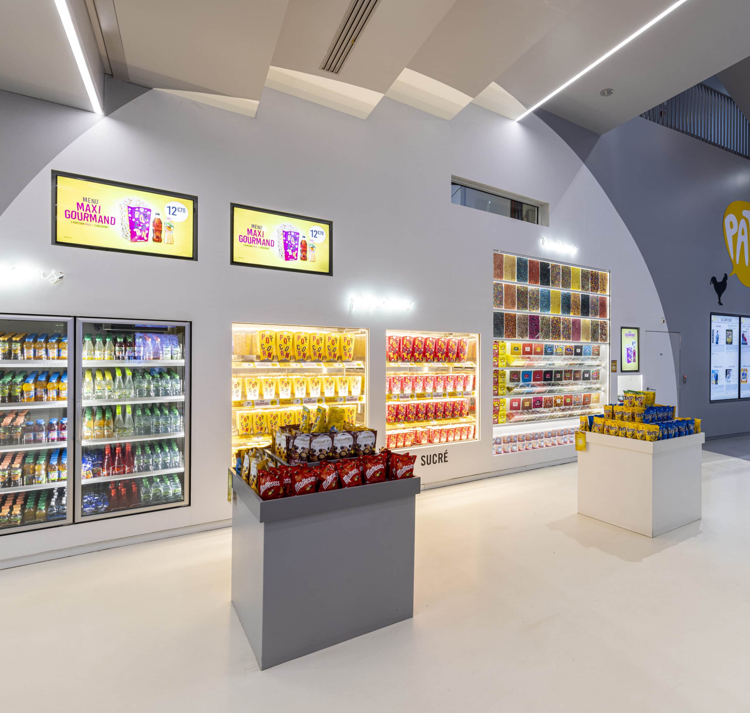 Espace confiserie du cinéma Pathé avec comptoir de pop-corn, distributeurs de boissons en libre-service et îlots de snacks et confiseries.