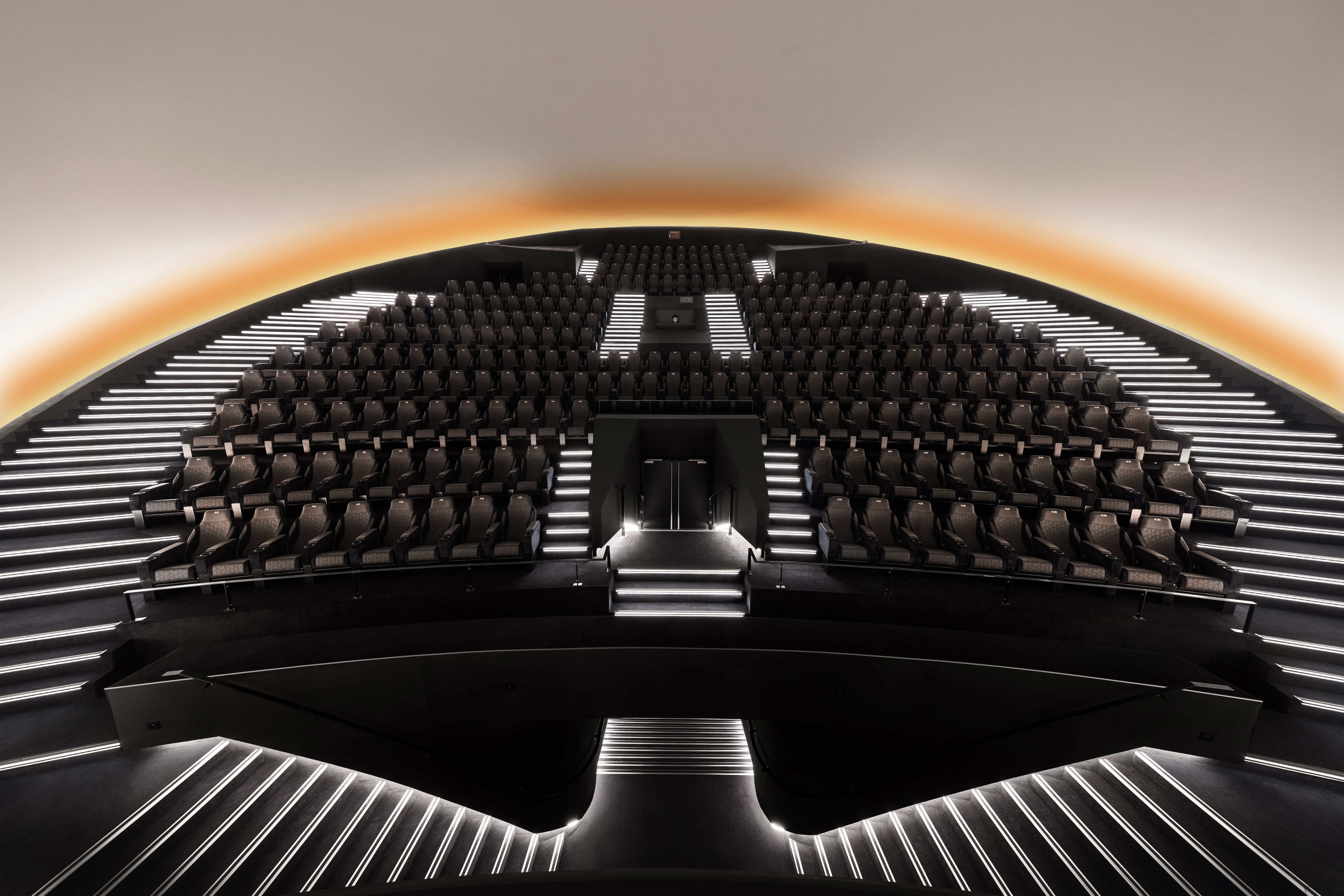 Salle de projection immersive avec sièges disposés en arc de cercle. Les escaliers rétroéclairés créent une atmosphère moderne, tandis que le plafond arrondi ajoute à l’expérience unique du lieu.