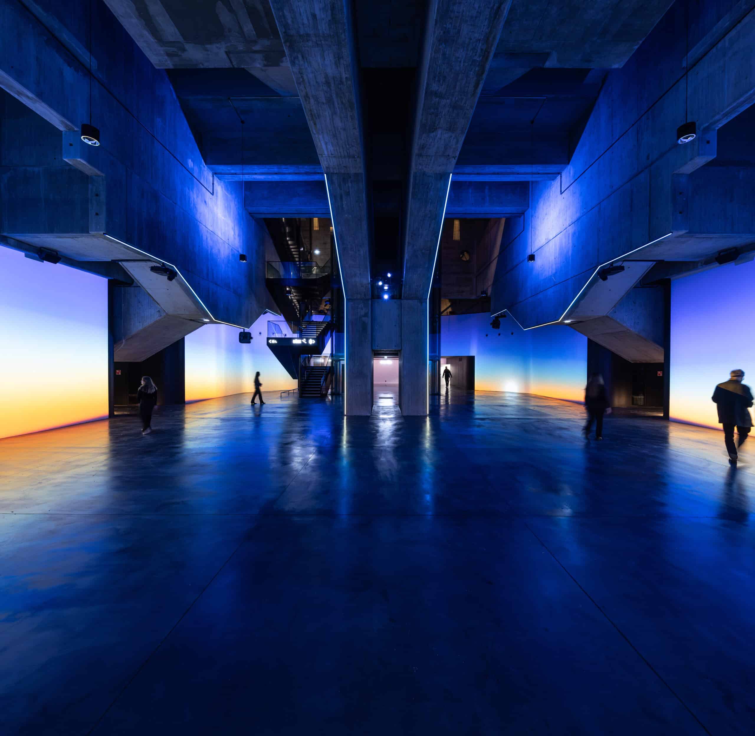 Espace cocktail du cinéma avec une grande hauteur sous plafond et entouré d'écran lumineux personnalisables.