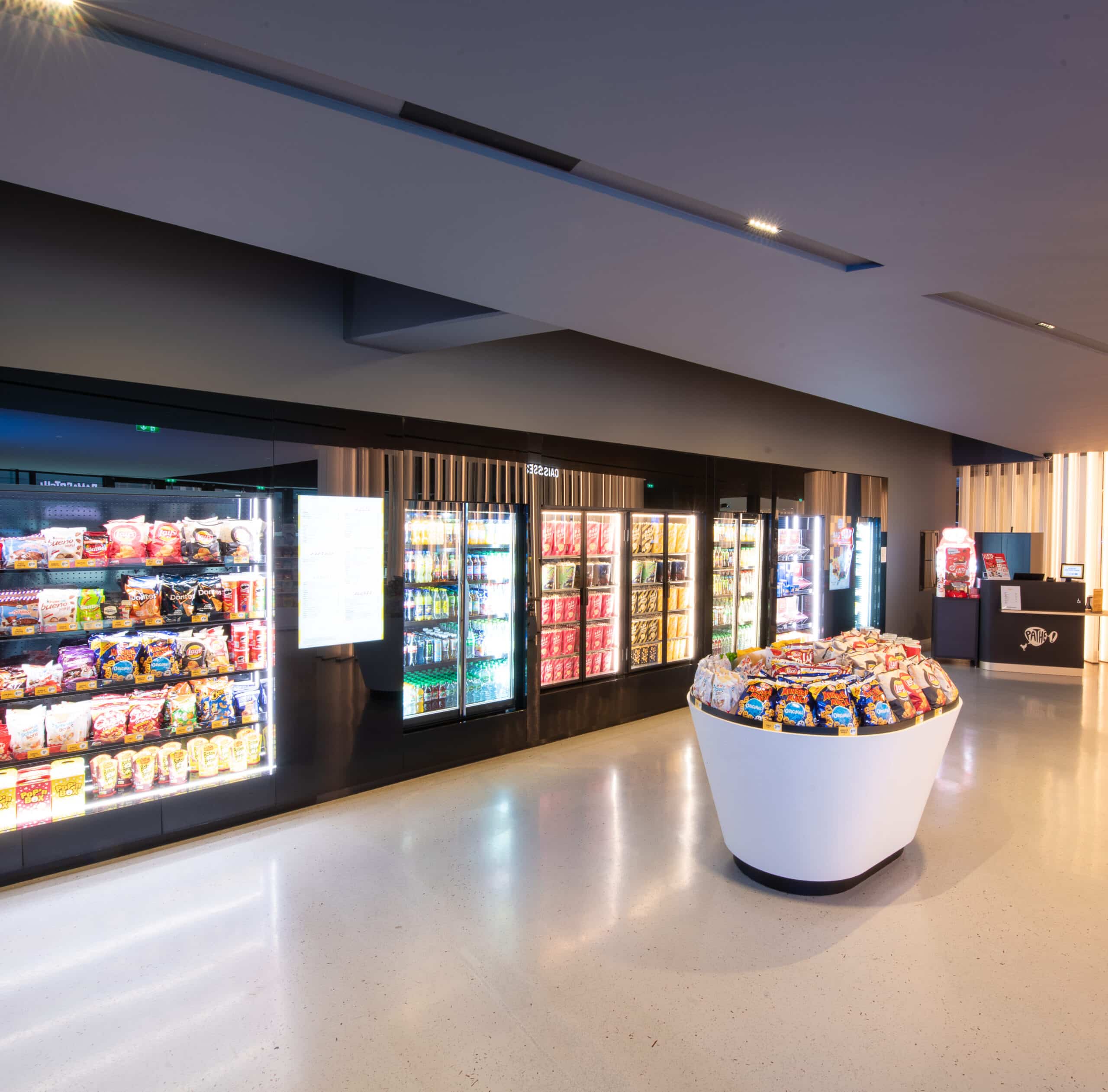 Espace confiserie du cinéma Pathé avec comptoir de pop-corn, distributeurs de boissons en libre-service et îlots de snacks et confiseries.