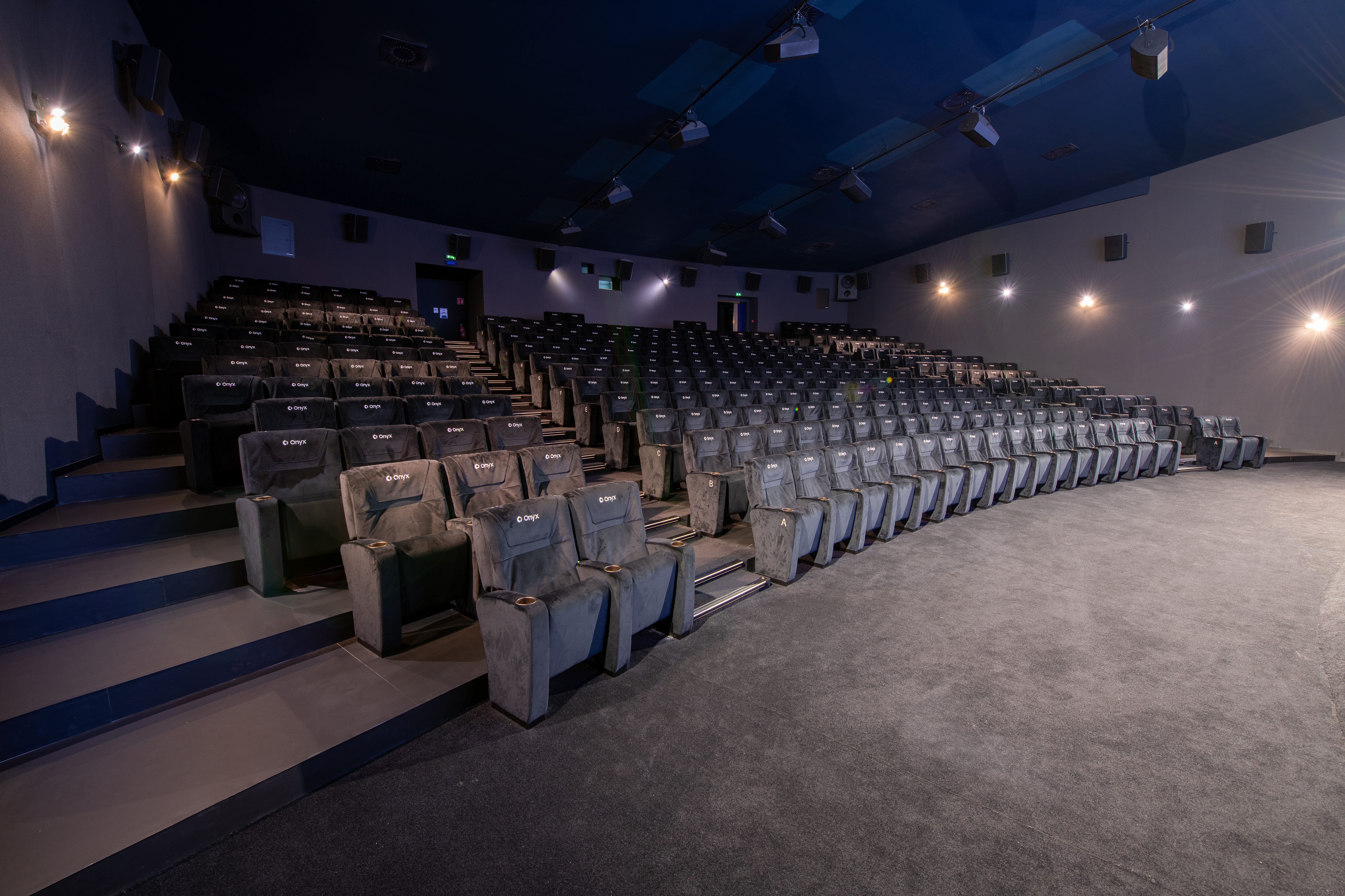 Grande salle de cinéma équipée de fauteuils en velours noir et de la technologie Onyx.
