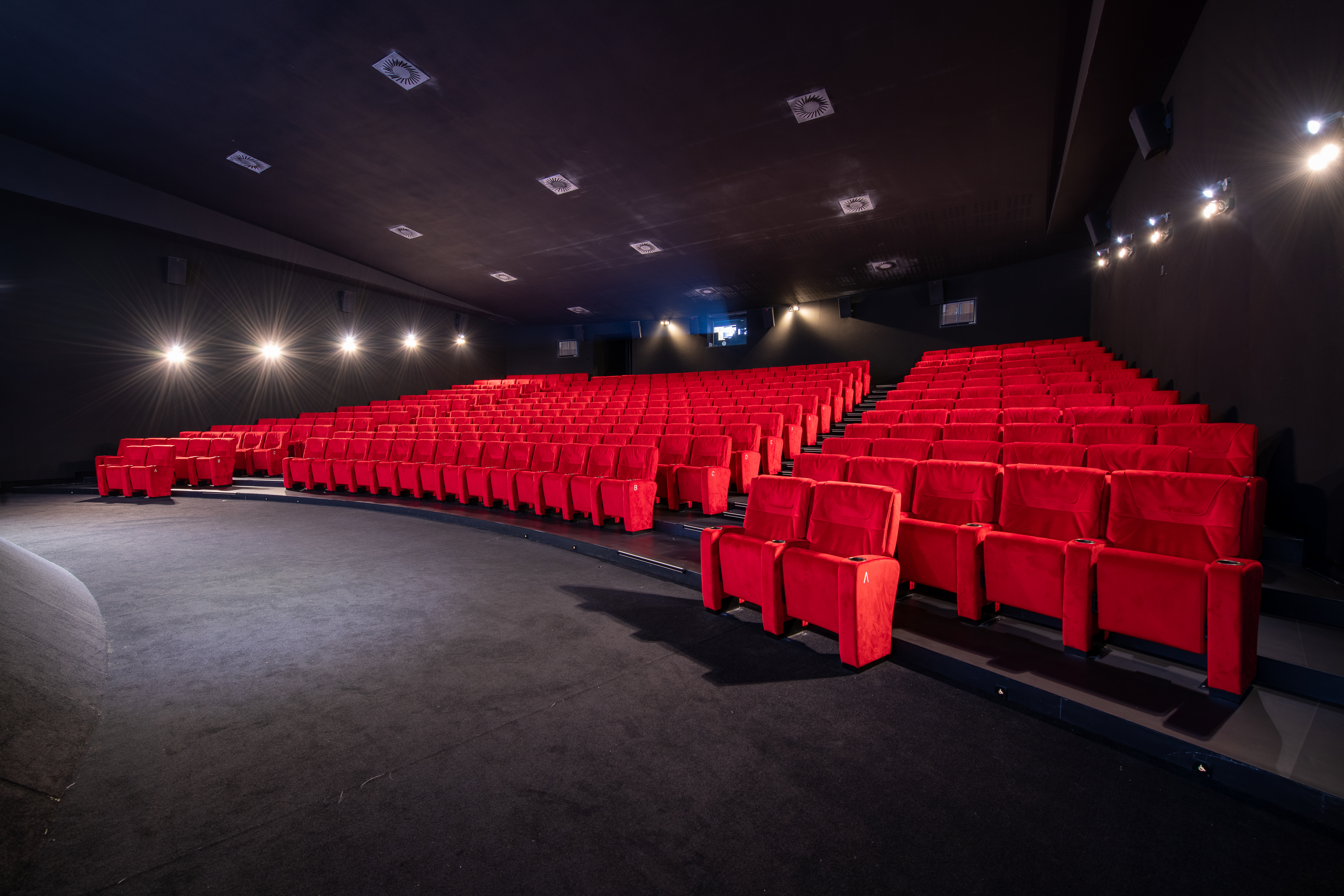 Salle de cinéma spacieuse avec rangées de fauteuils rouges, éclairage discret sur les murs et ambiance feutrée idéale pour les projections