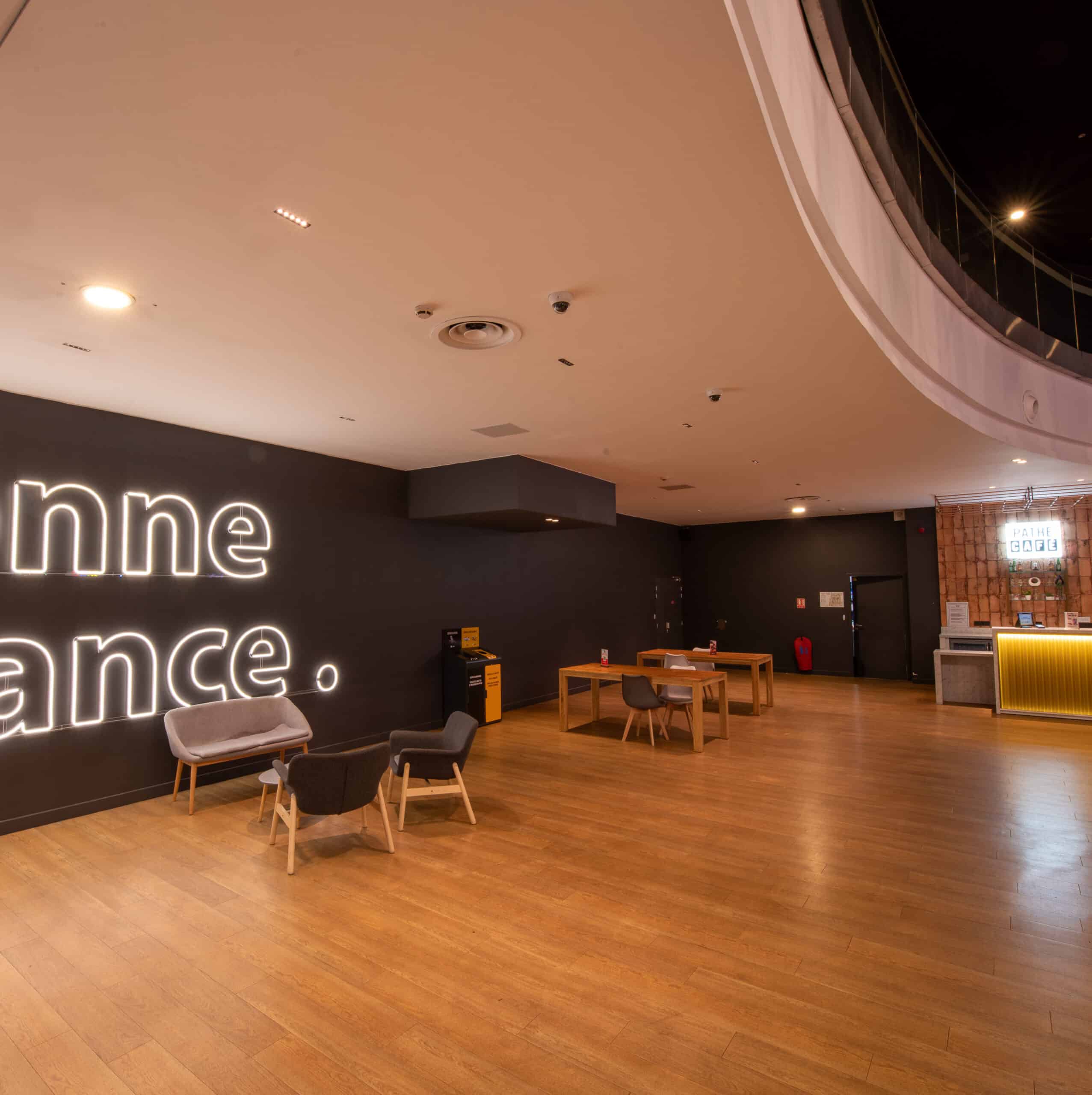 Espace de réception situé dans le hall du cinéma, éclairé par des lumières chaudes avec du mobilier de réception gris.