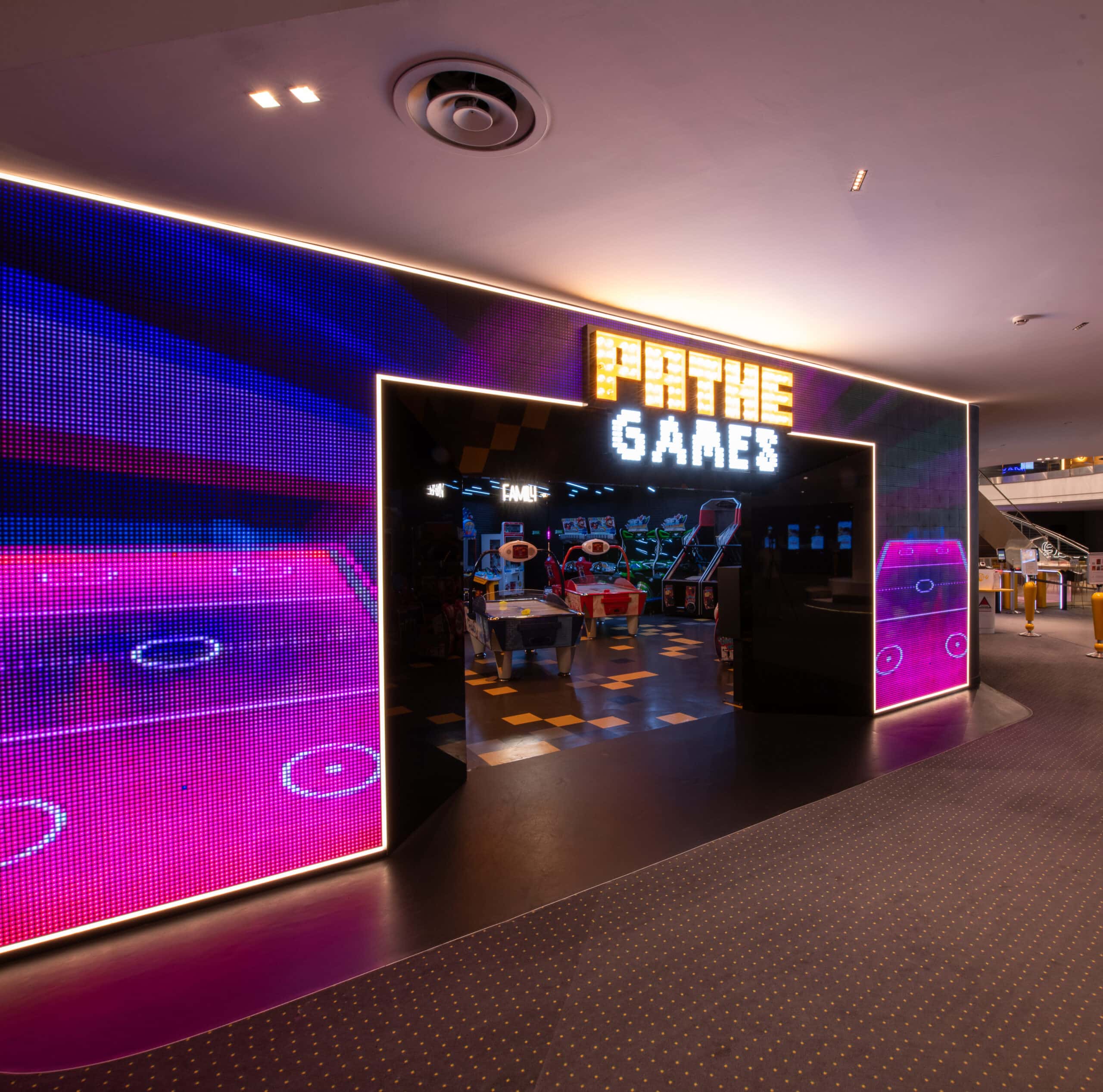 Espace Pathé Games avec différentes machines d’arcade et de jeux vidéo, éclairage néon coloré, ambiance moderne et ludique, proposant des jeux pour tous les âges dans un cadre convivial.