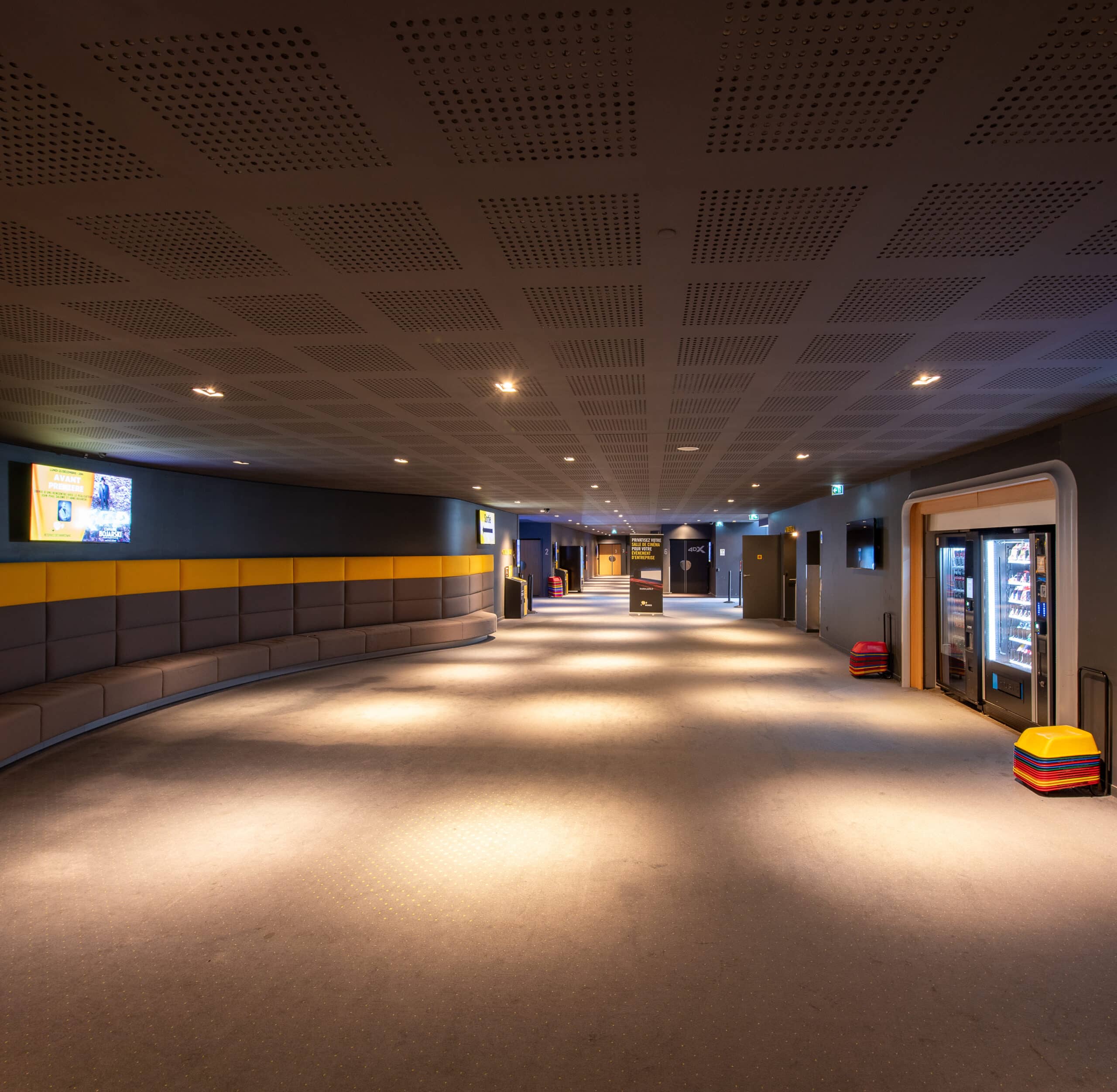 Espace de réception situé dans le hall du cinéma, éclairé par une lumière tamisée et aménagé avec des canapés et du mobilier de salon.