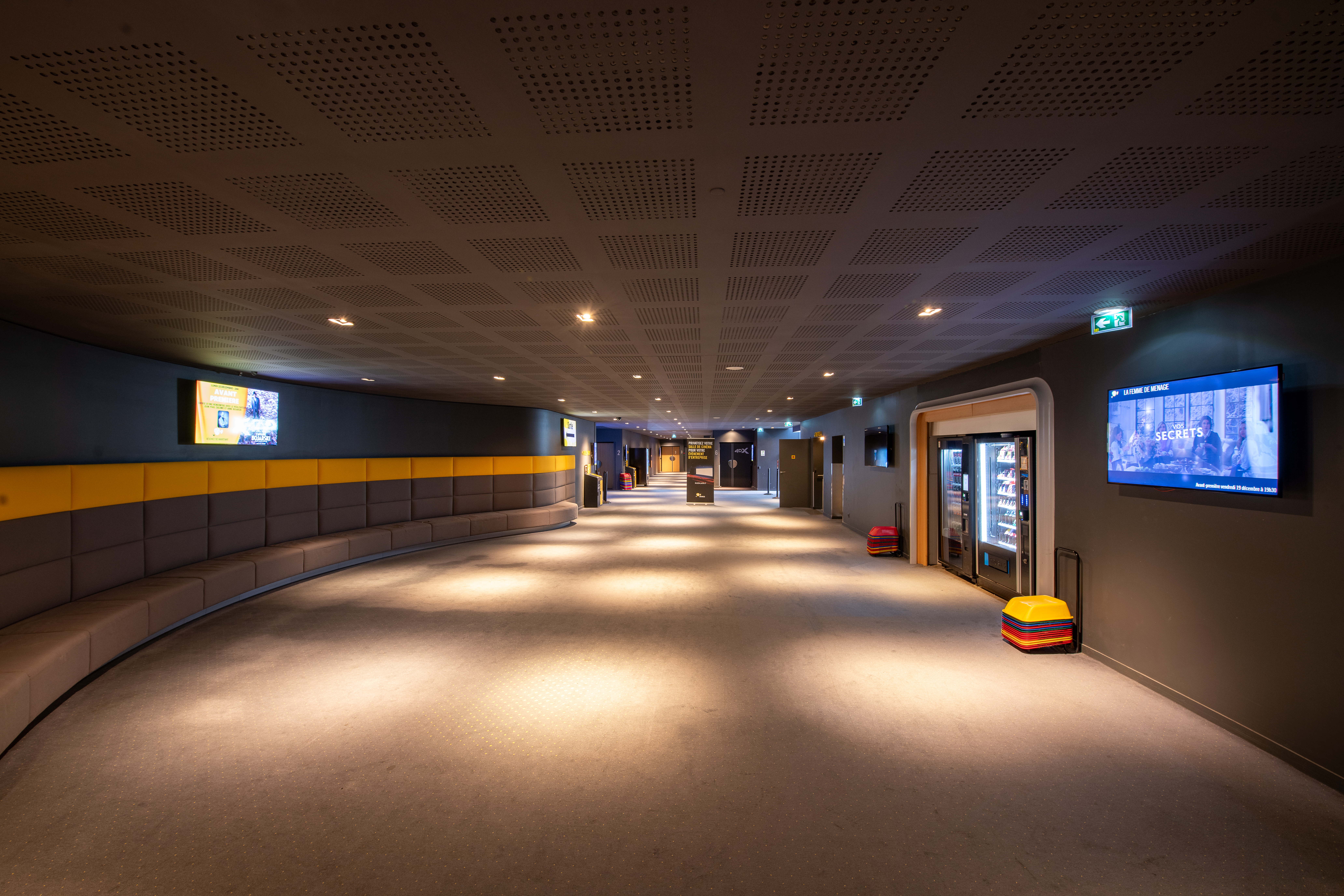 Espace de réception situé dans le hall du cinéma, éclairé par une lumière tamisée et aménagé avec des canapés et du mobilier de salon.