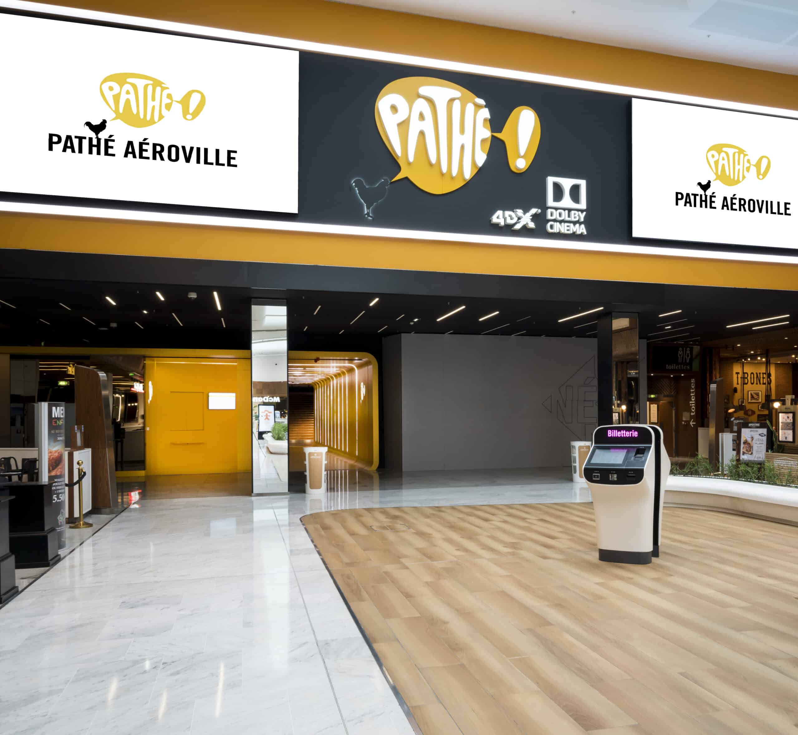 Entrée du cinéma Pathé Aéroville avec affichages lumineux, bornes de billetterie et design moderne jaune et noir.