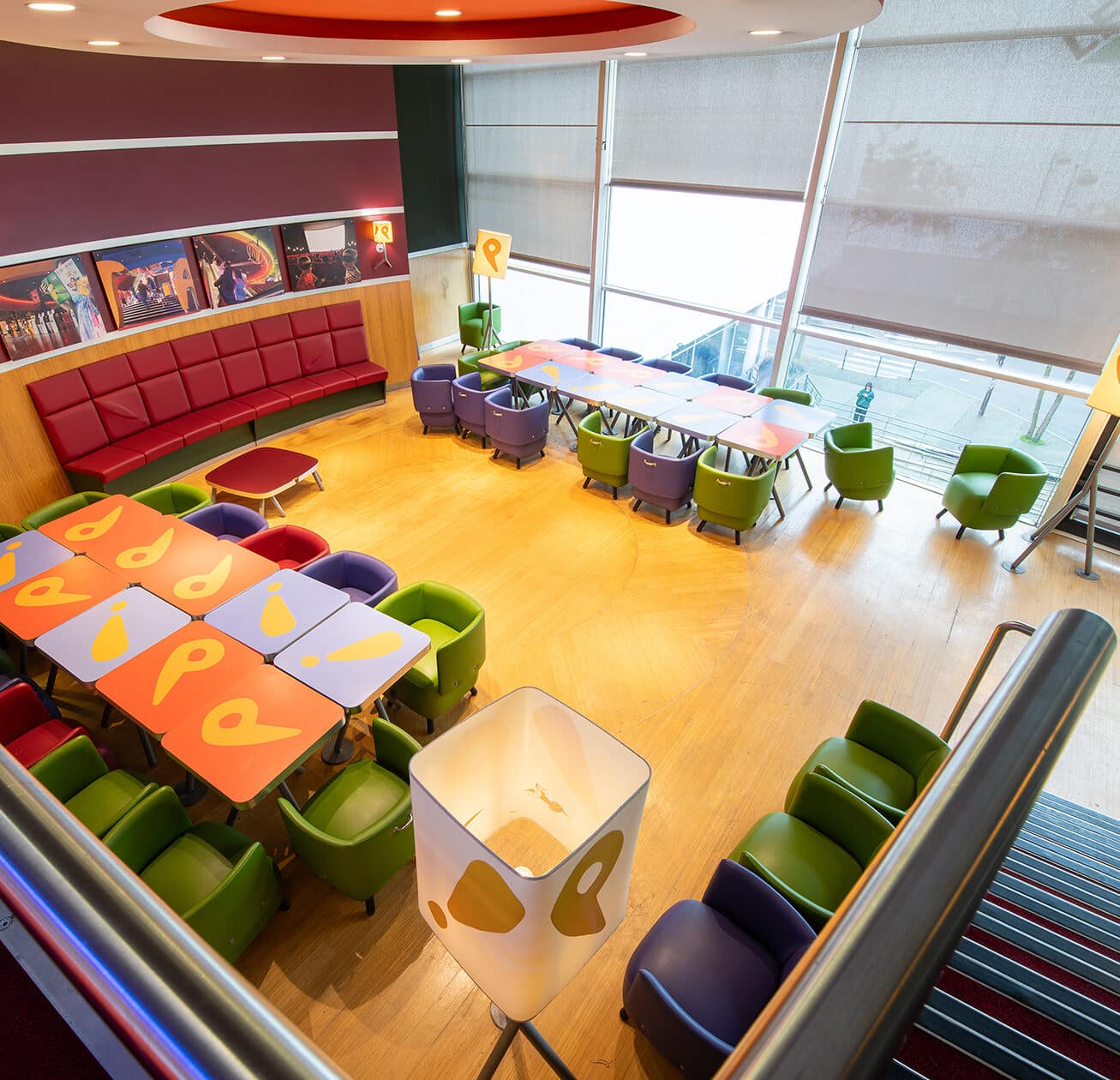Espace cocktail du cinéma, éclairé par des lumières colorées et aménagé avec du mobilier de réception vert et violet.