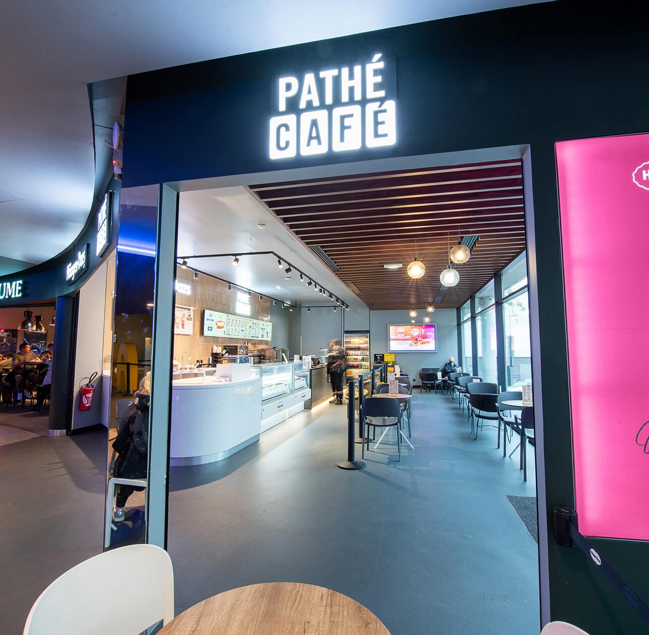Entrée du Pathé Café avec enseigne lumineuse, comptoirs modernes, tables et chaises dans un espace lumineux.