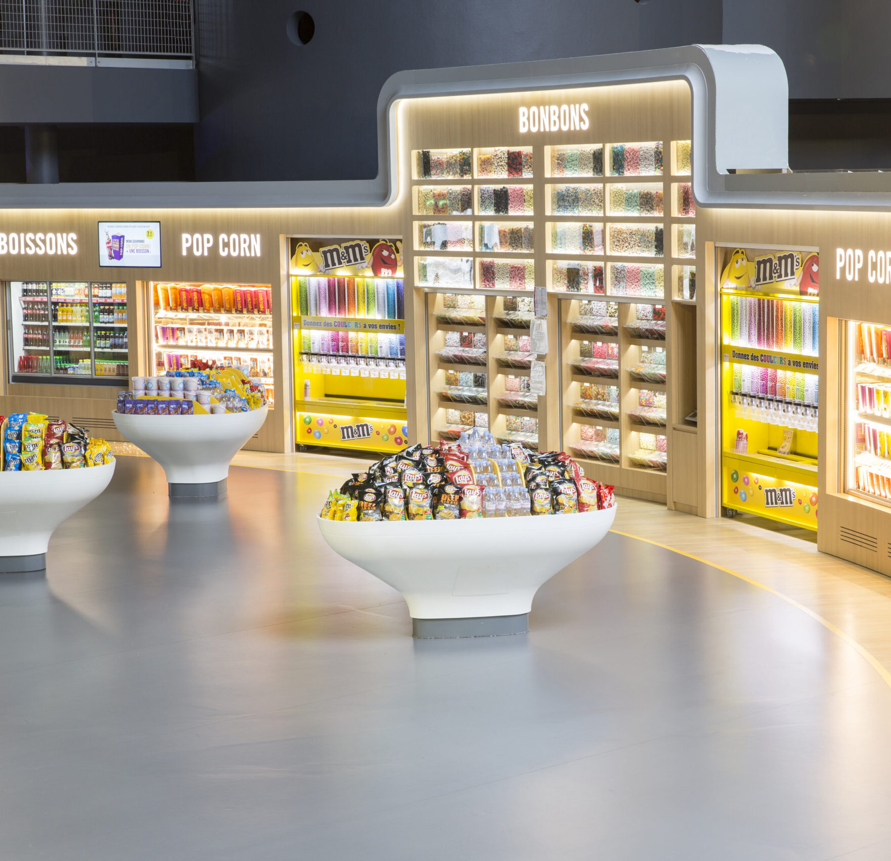 Espace confiserie du cinéma Pathé avec comptoir de pop-corn, distributeurs de boissons en libre-service et îlots de snacks et confiseries.