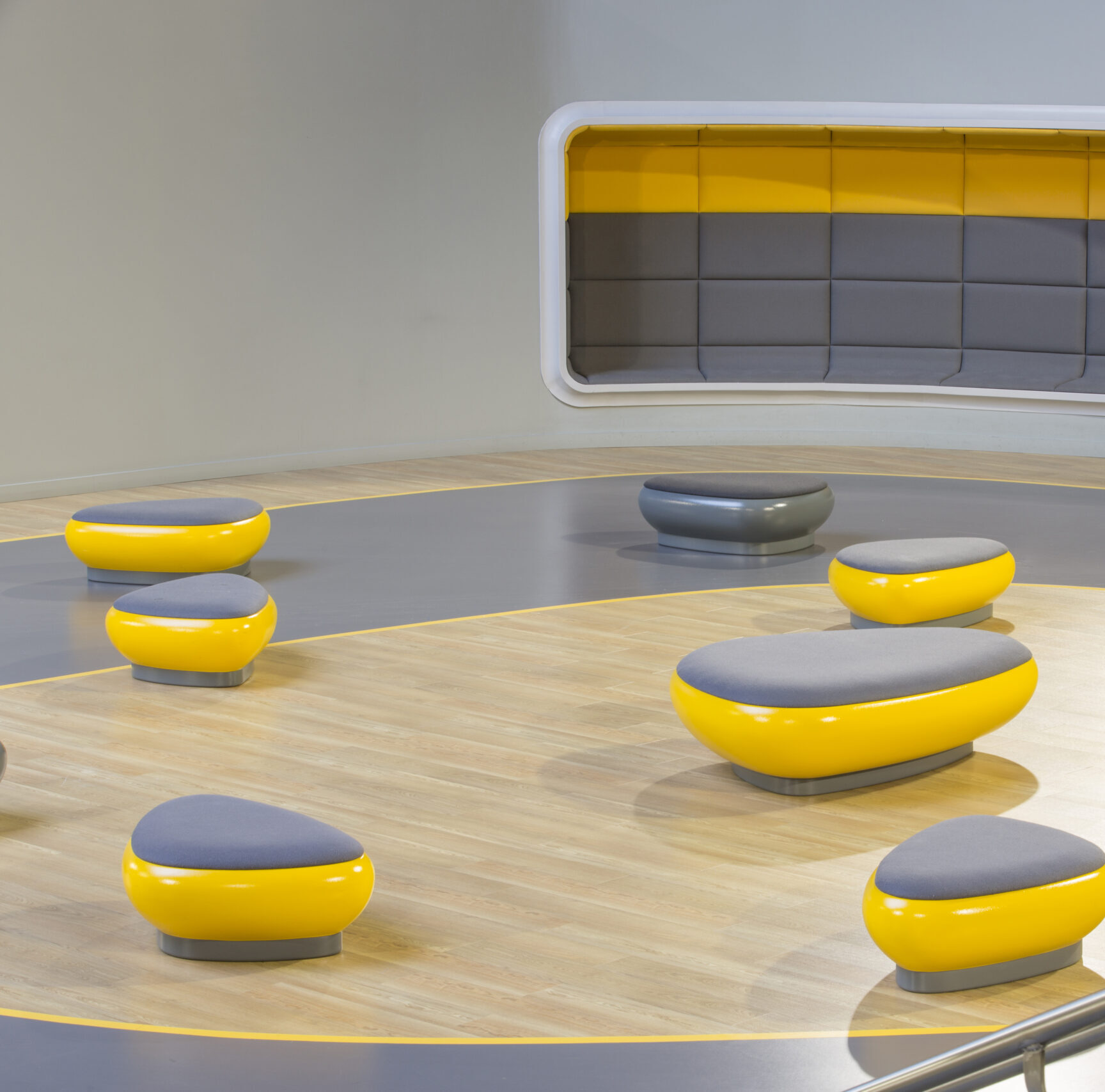 Zone d'assise moderne dans un cinéma avec des poufs arrondis jaunes et gris sur un sol clair, et un canapé intégré dans le mur.