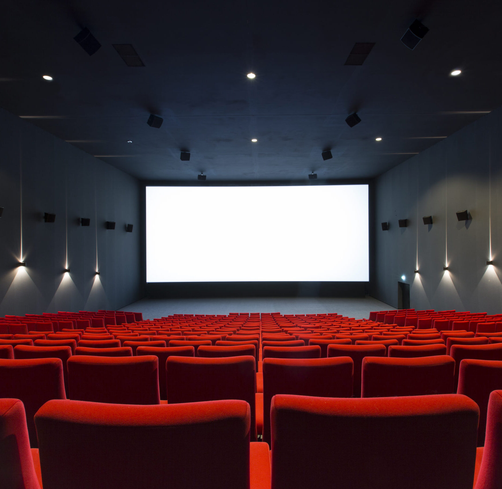 Vue depuis l’arrière d'une salle du cinéma Pathé avec ses rangées de fauteuils en velours rouges orientés vers l’écran.
