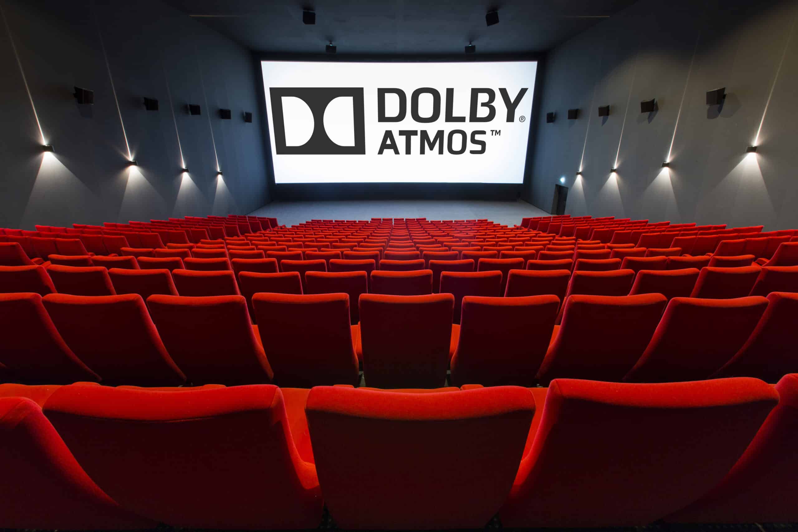 Vue de derrière d'une salle de cinéma équipée de la technologie Dolby Atmos montrant les fauteuils en velours rouges et l’agencement des rangées ainsi que son espace scénique.