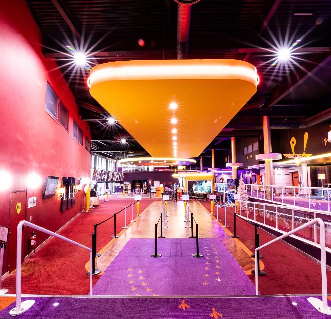 Hall du cinéma avec tapis violet, éclairage lumineux suspendu et ambiance festive.