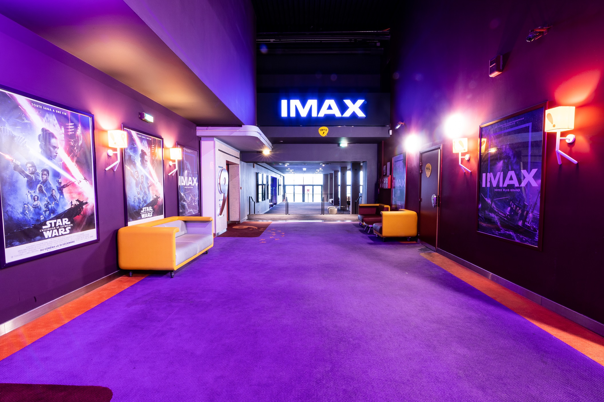 Hall d'entrée pour l'expérience IMAX du cinéma, avec affiches, éclairage violet et fauteuils modernes.