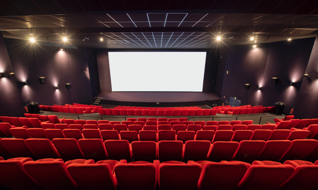 Vue depuis l’arrière d'une salle du cinéma Pathé avec ses rangées de fauteuils en velours rouges orientés vers l’écran.