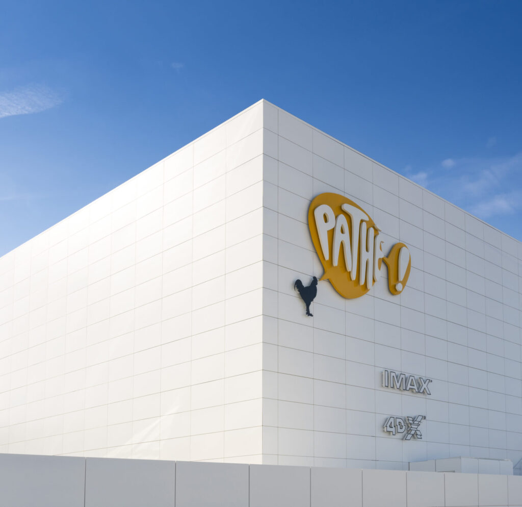 Façade extérieure du cinéma à la lumière du jour avec le logo Pathé apparent et un ciel bleu en arrière plan.