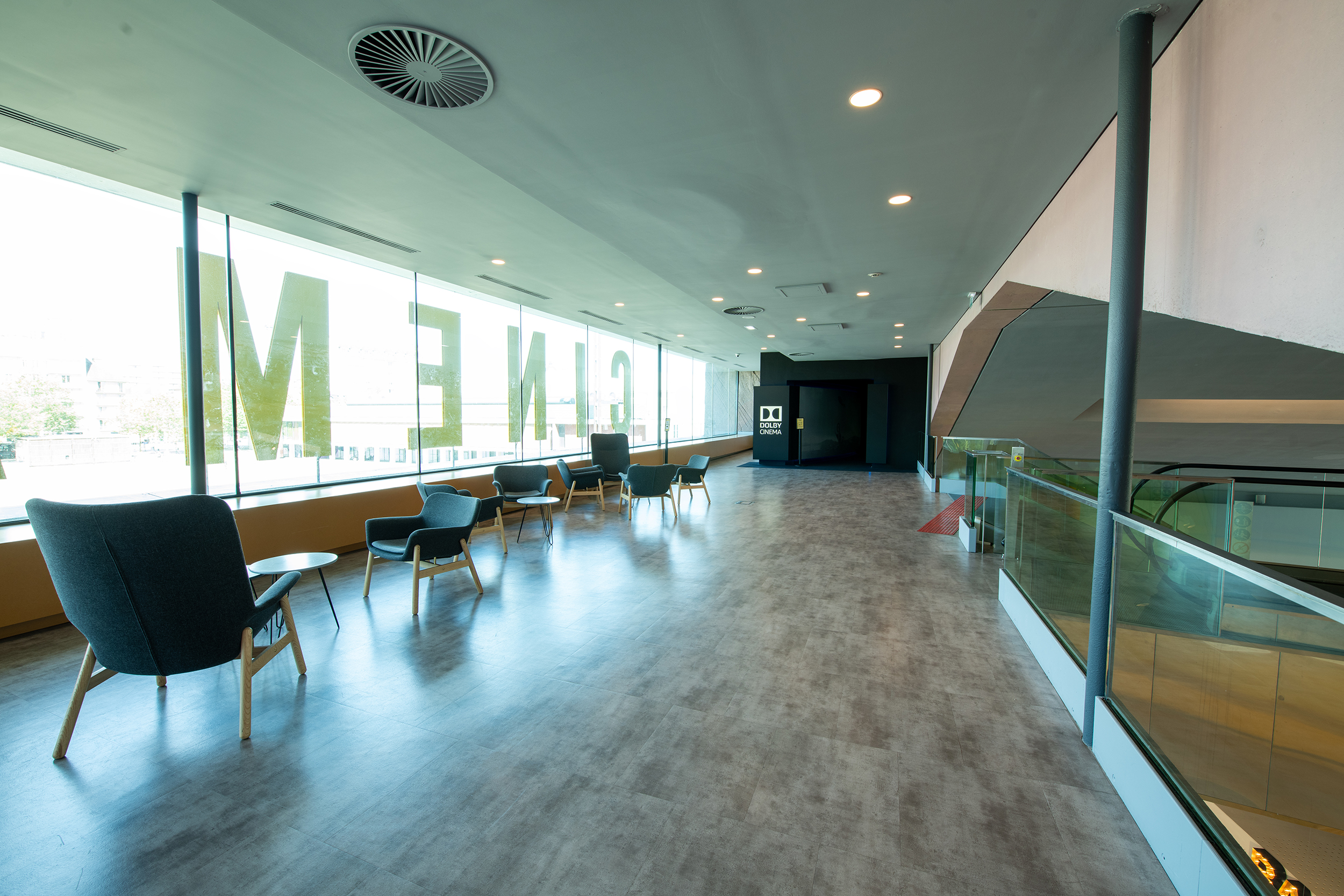 Espace lumineux du cinéma avec fauteuils modernes, vue sur l'extérieur et accès à la salle Dolby Cinema.