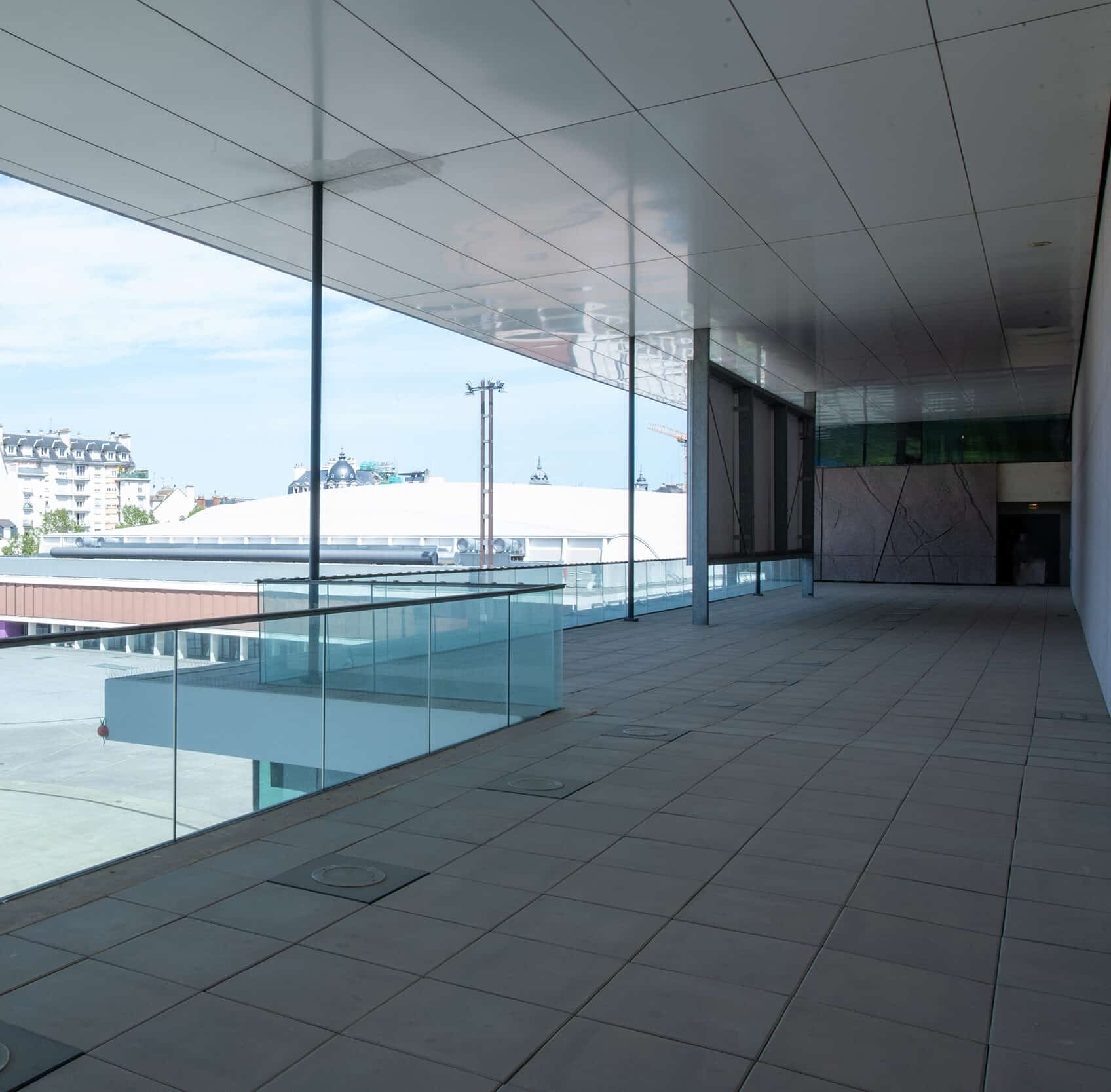 Terrasse couverte du cinéma avec garde-corps en verre et vue sur les bâtiments environnants.