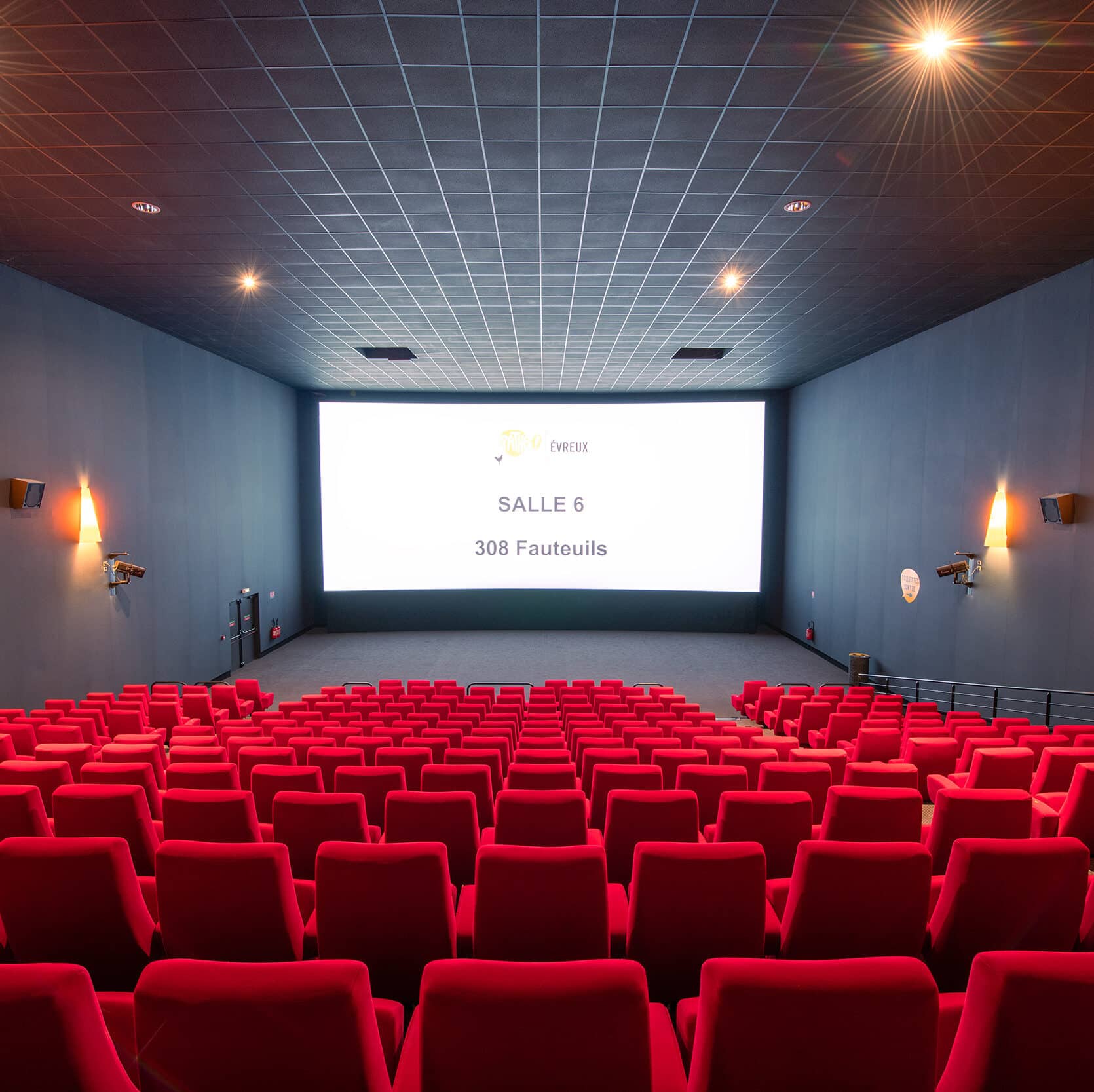 Vue depuis l’arrière de la salle 6 du cinéma Pathé Evreux avec rangées de fauteuils en velours rouges orientés vers l’écran.