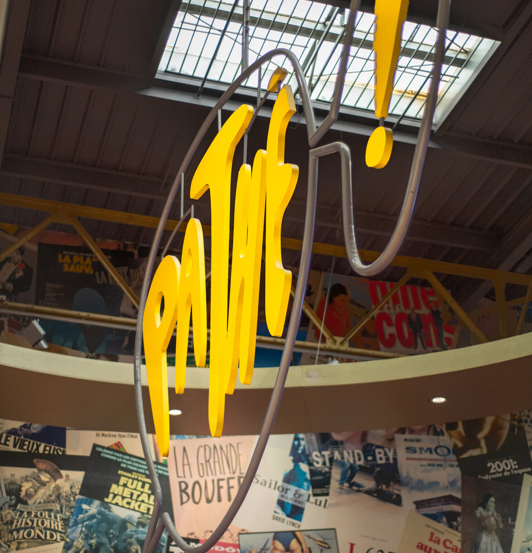 Logo lumineux « Pathé ! » suspendu au-dessus d'un espace décoré avec des affiches de films cultes.