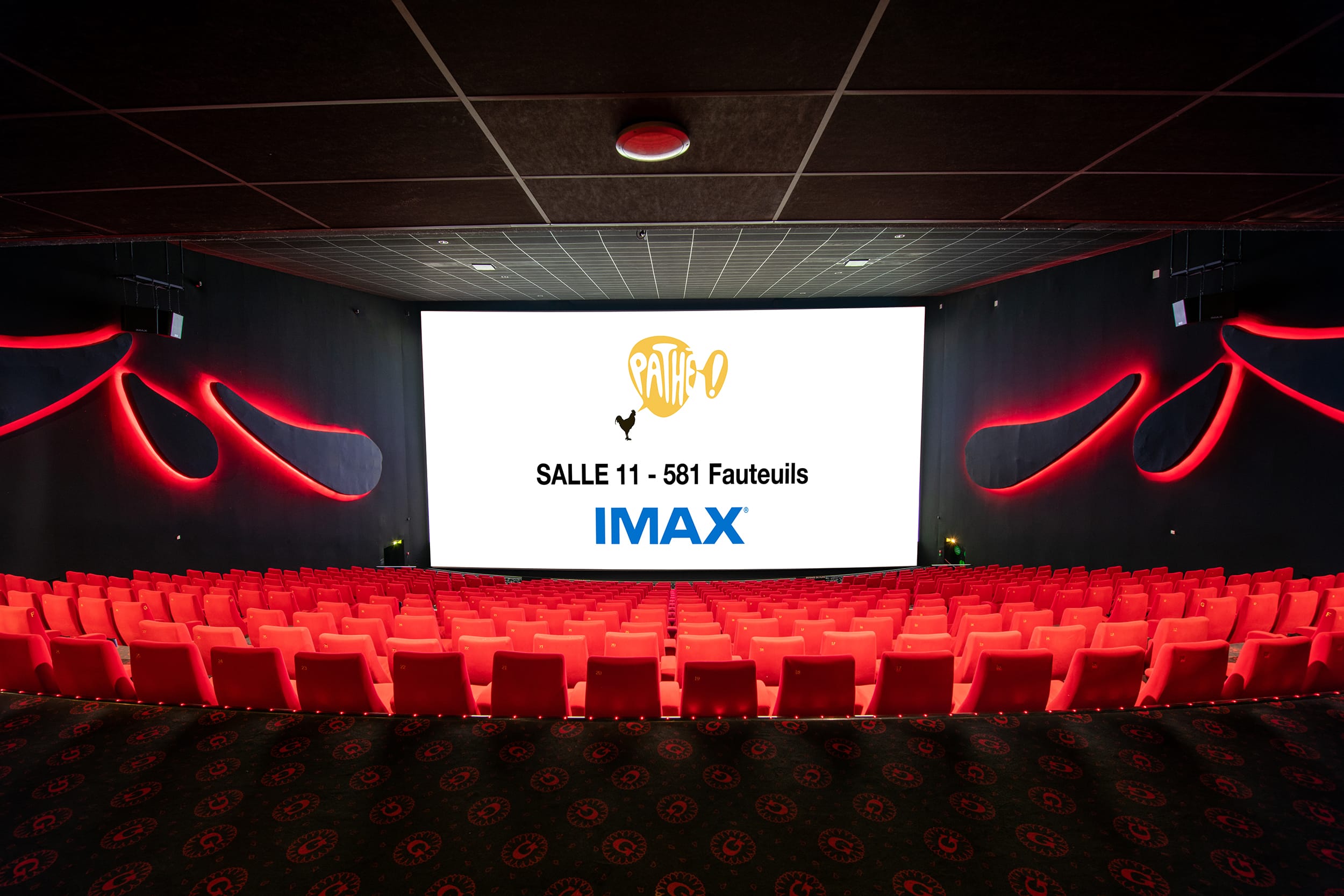 Vue depuis l’arrière d'une salle de cinéma avec la technologie IMAX et ses rangées de fauteuils en velours rouges orientés vers l’écran.
