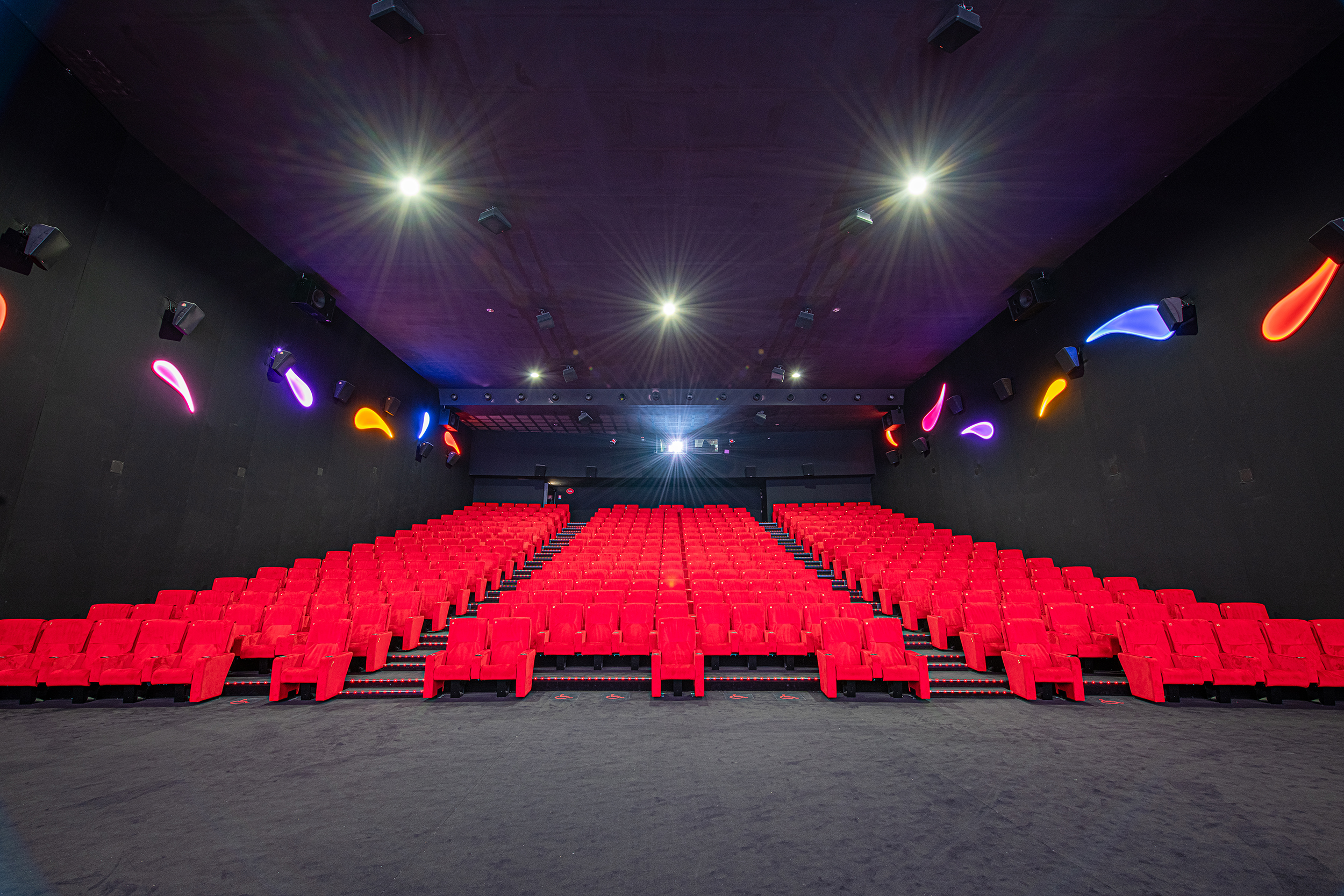 Vu d'ensemble de face d'une grande salle de cinéma Pathé avec ses fauteuils en velours rouge et ses spots lumineux qui éclairent la salle.