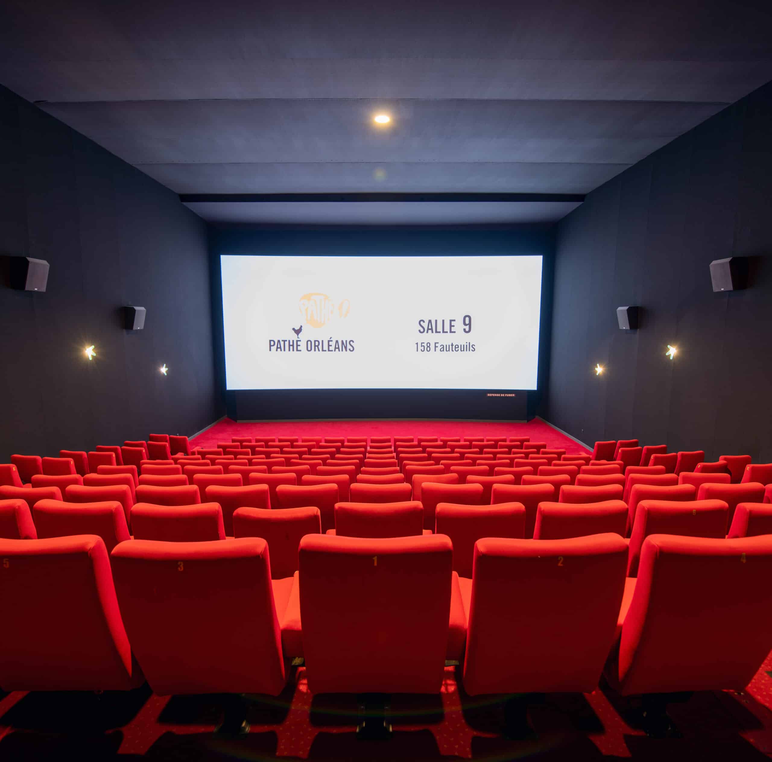 Vue depuis l’arrière de la salle 9 du cinéma Pathé Orléans avec rangées de fauteuils en velours rouges orientés vers l’écran.