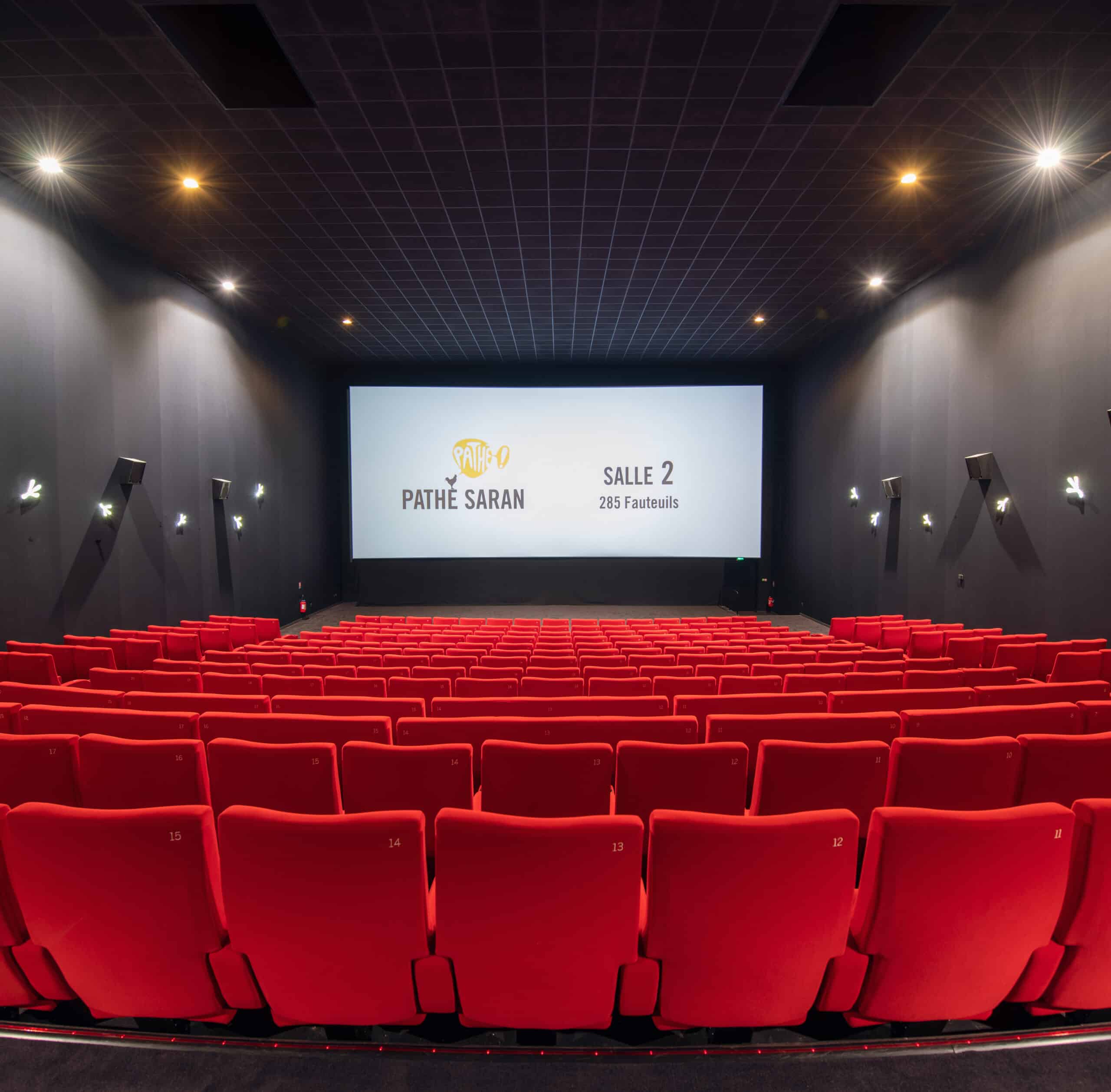 Vue depuis l’arrière de la salle 2 du cinéma Pathé Saran avec rangées de fauteuils en velours rouges orientés vers l’écran.