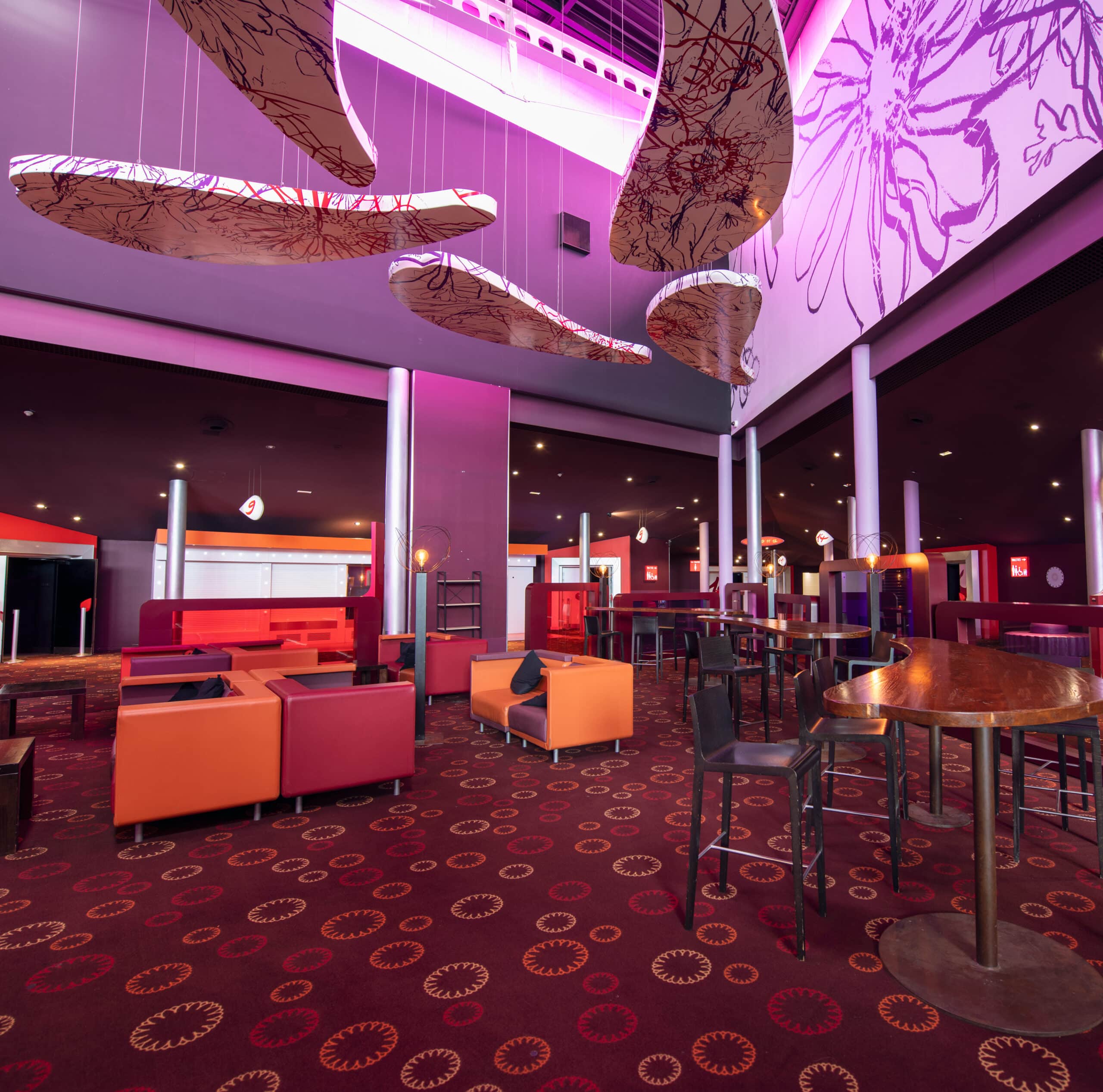 Espace lounge du cinéma avec mobilier coloré, décorations suspendues et éclairage rose immersif.