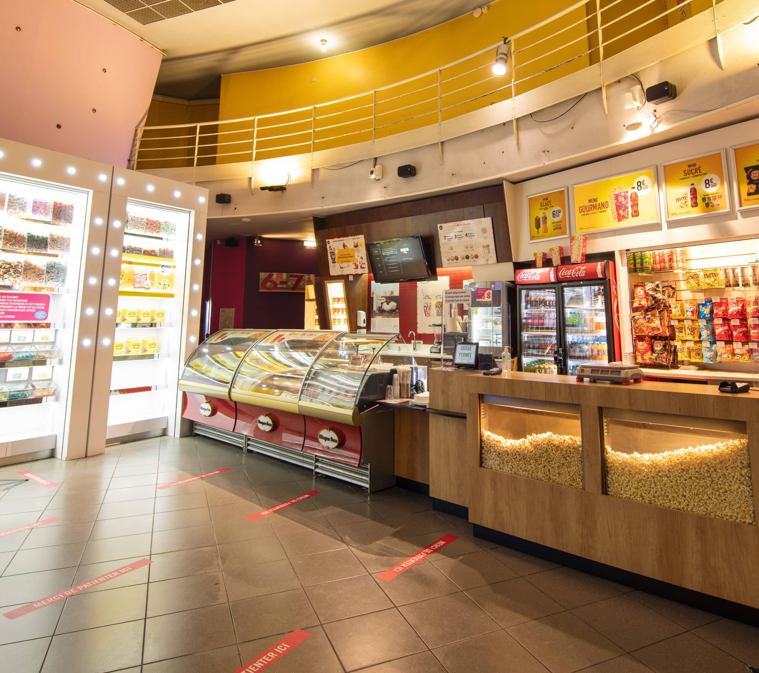Espace confiserie du cinéma Pathé avec comptoir de pop-corn, distributeurs de boissons en libre-service et îlots de snacks et confiseries.