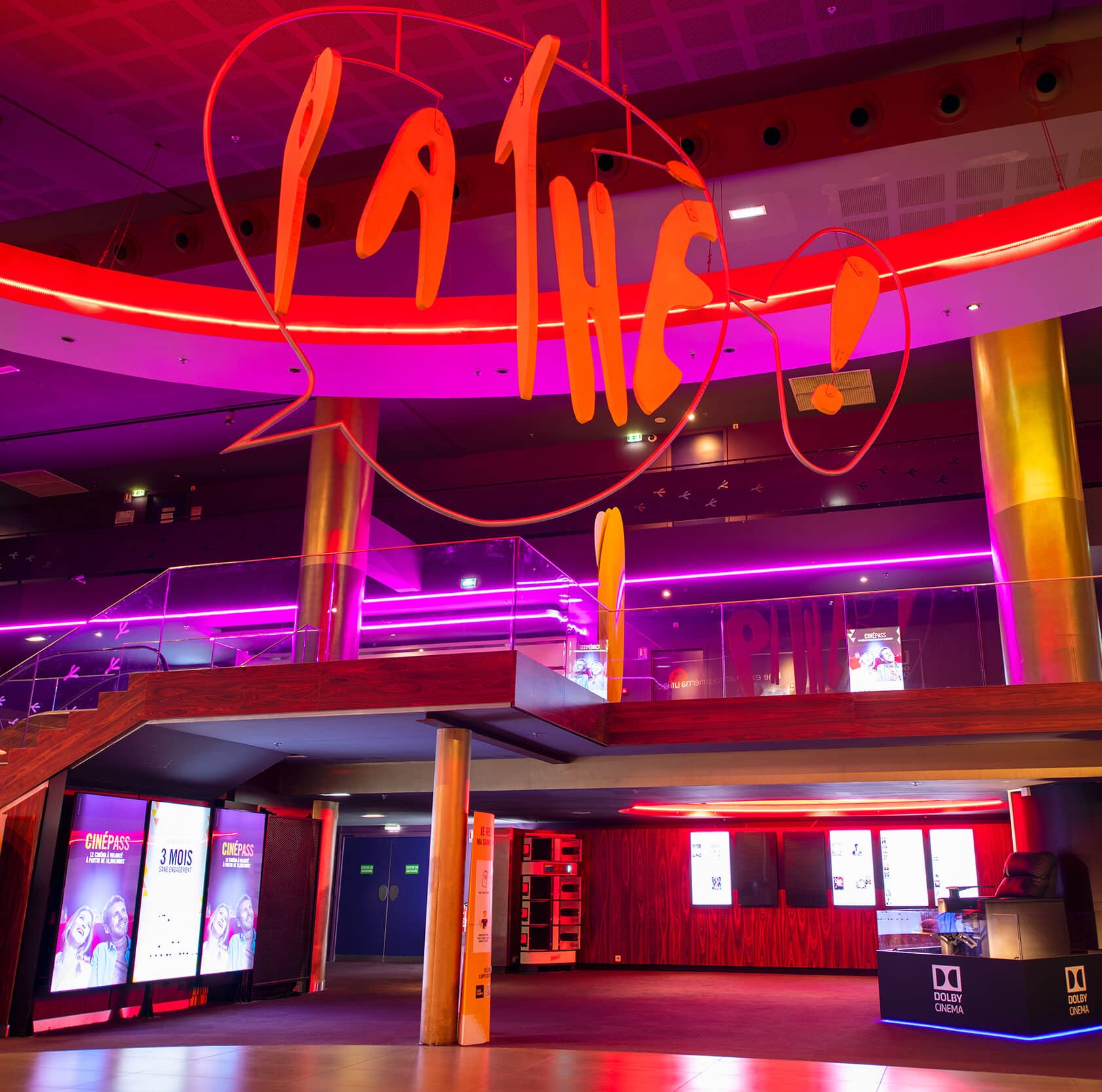 Logo « Pathé ! » suspendu dans un hall aux tons roses avec mezzanine et ambiance lumineuse moderne.