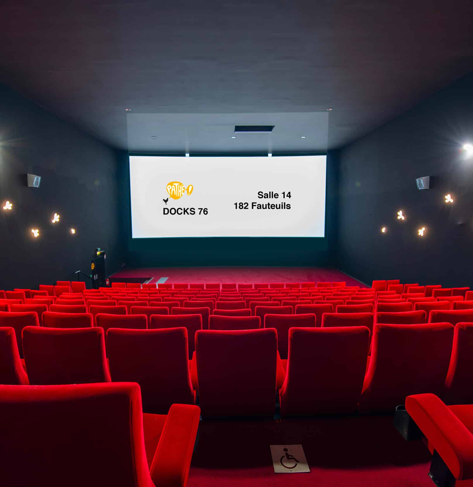 Vue depuis l’arrière de la salle 14 du cinéma Pathé Docks 76 avec rangées de fauteuils en velours rouges orientés vers l’écran.
