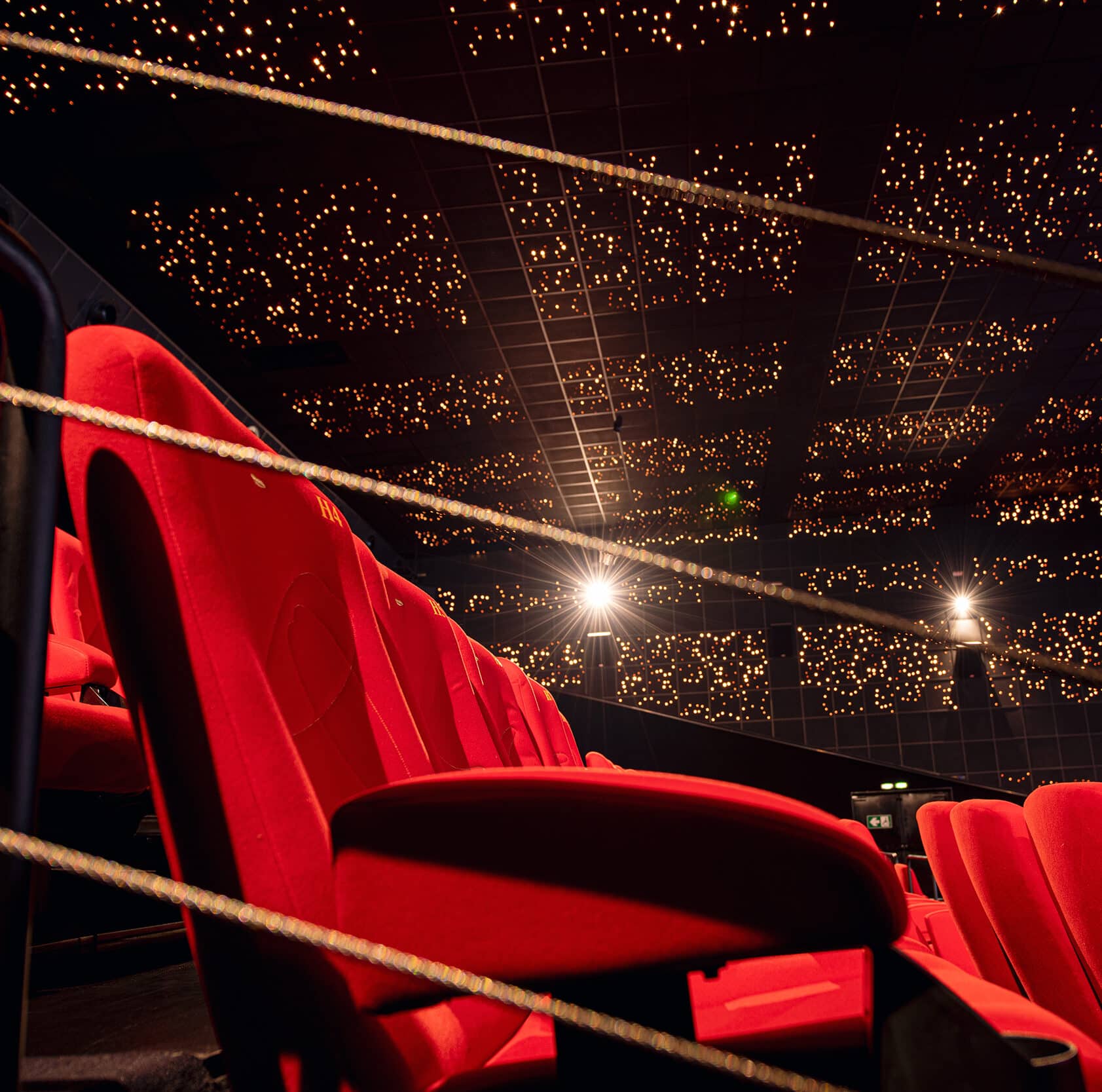 Salle de cinéma avec sièges rouges et plafond étoilé illuminé, créant une atmosphère immersive.