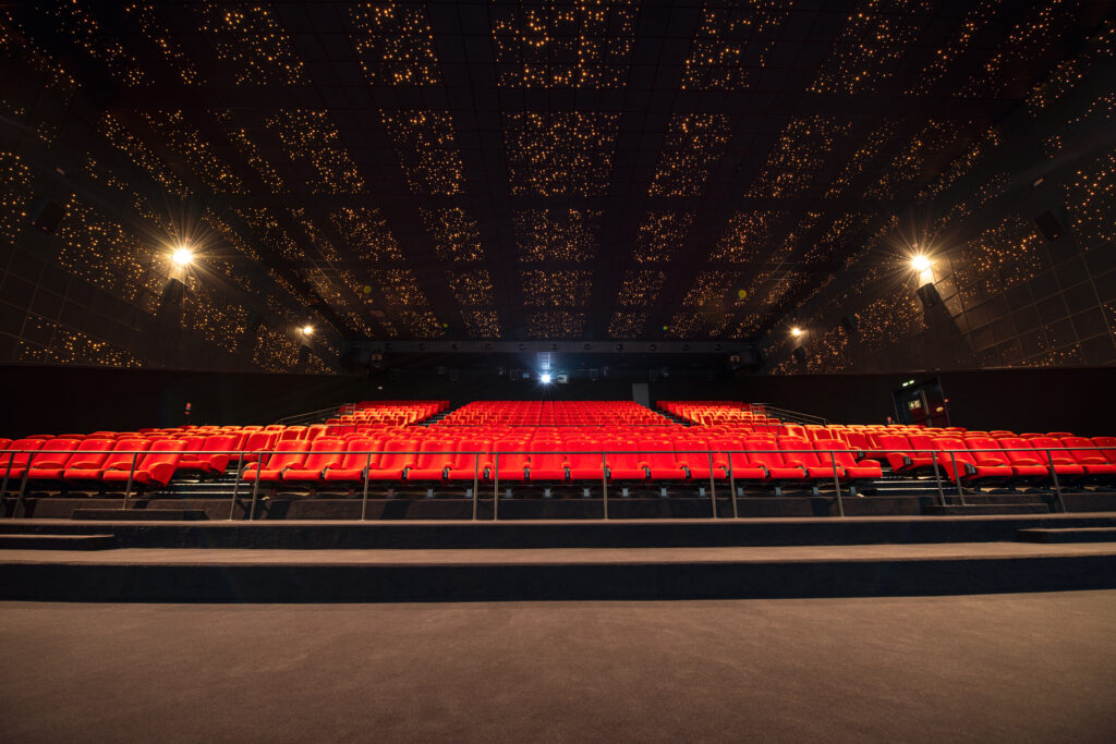 Vu d'ensemble de face d'une grande salle avec ses fauteuils en velours rouge.