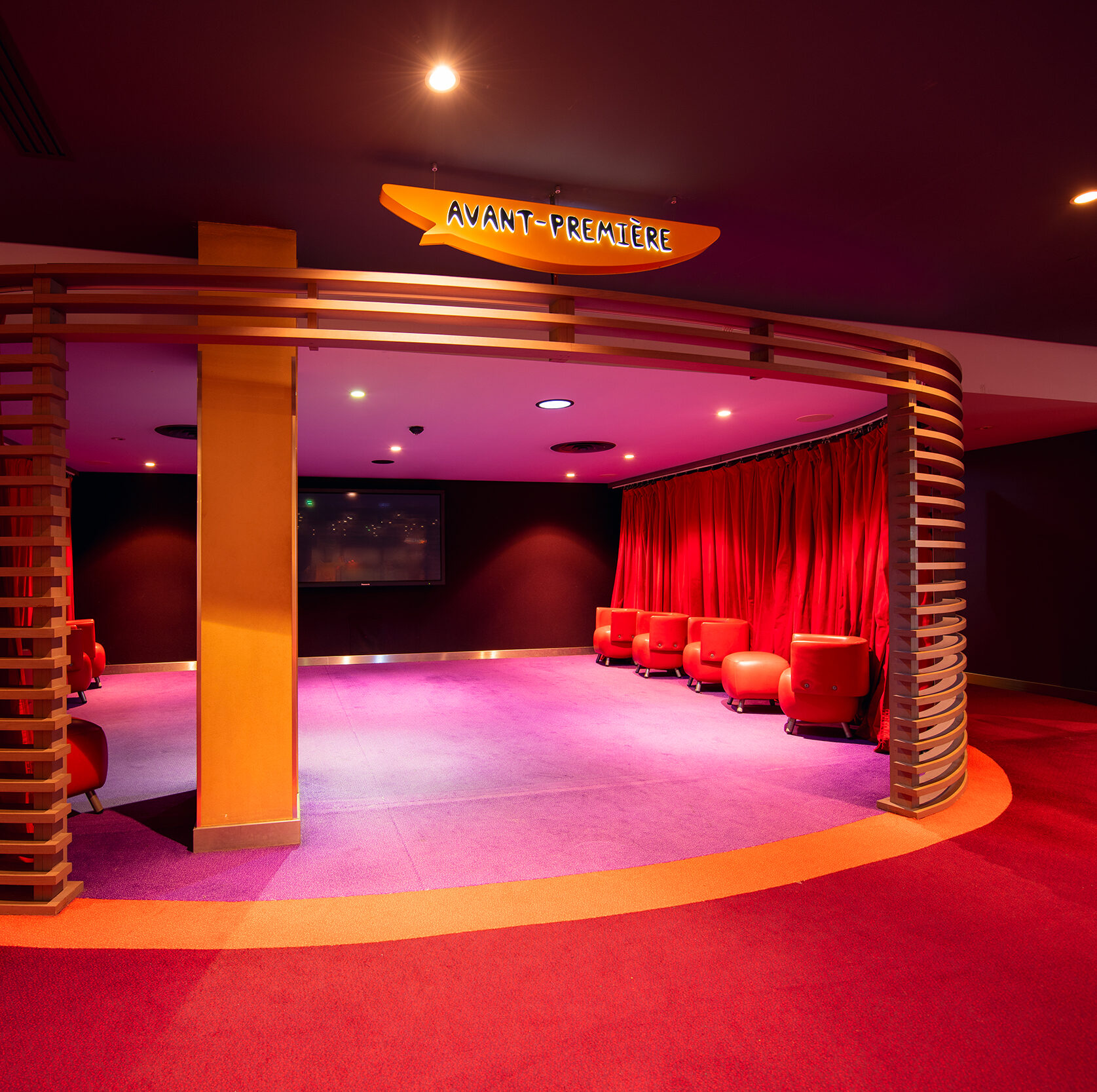 Espace de réception situé dans la continuité du hall du cinéma, éclairé par une lumière tamisée et aménagé avec des canapés et du mobilier de salon.
