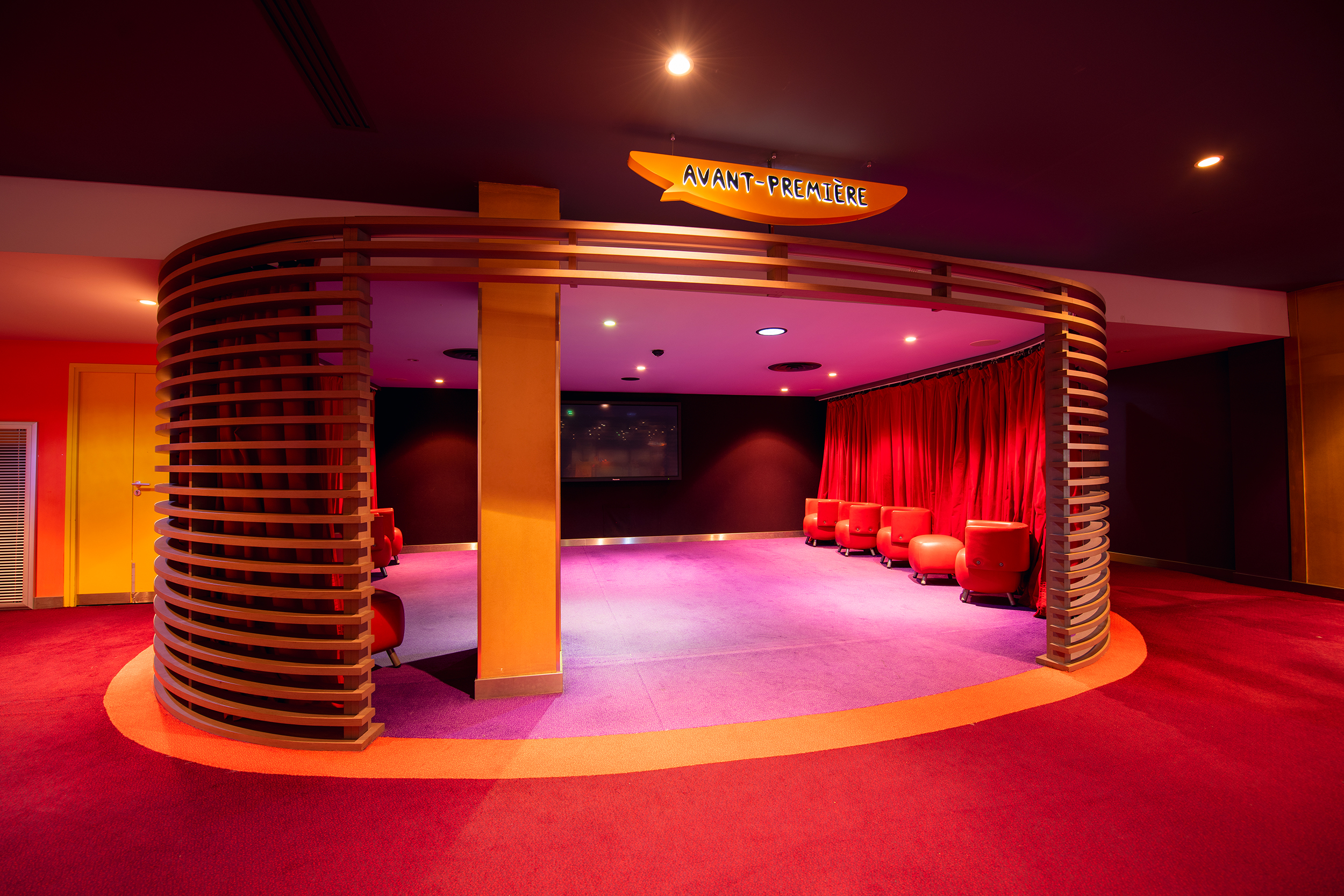 Espace de réception situé dans la continuité du hall du cinéma, éclairé par une lumière tamisée et aménagé avec des canapés et du mobilier de salon.