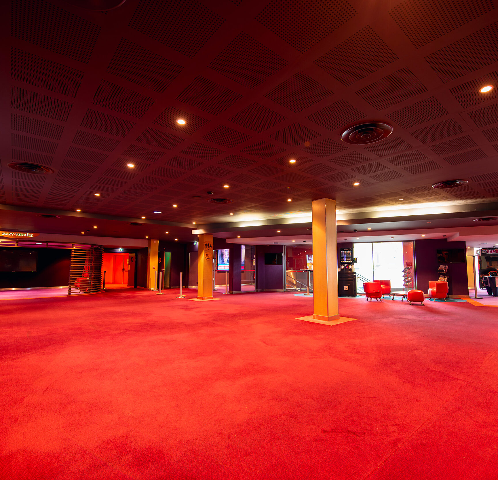 Grand espace de réception situé dans le hall du cinéma, éclairé par une lumière tamisée et des tons rouges.