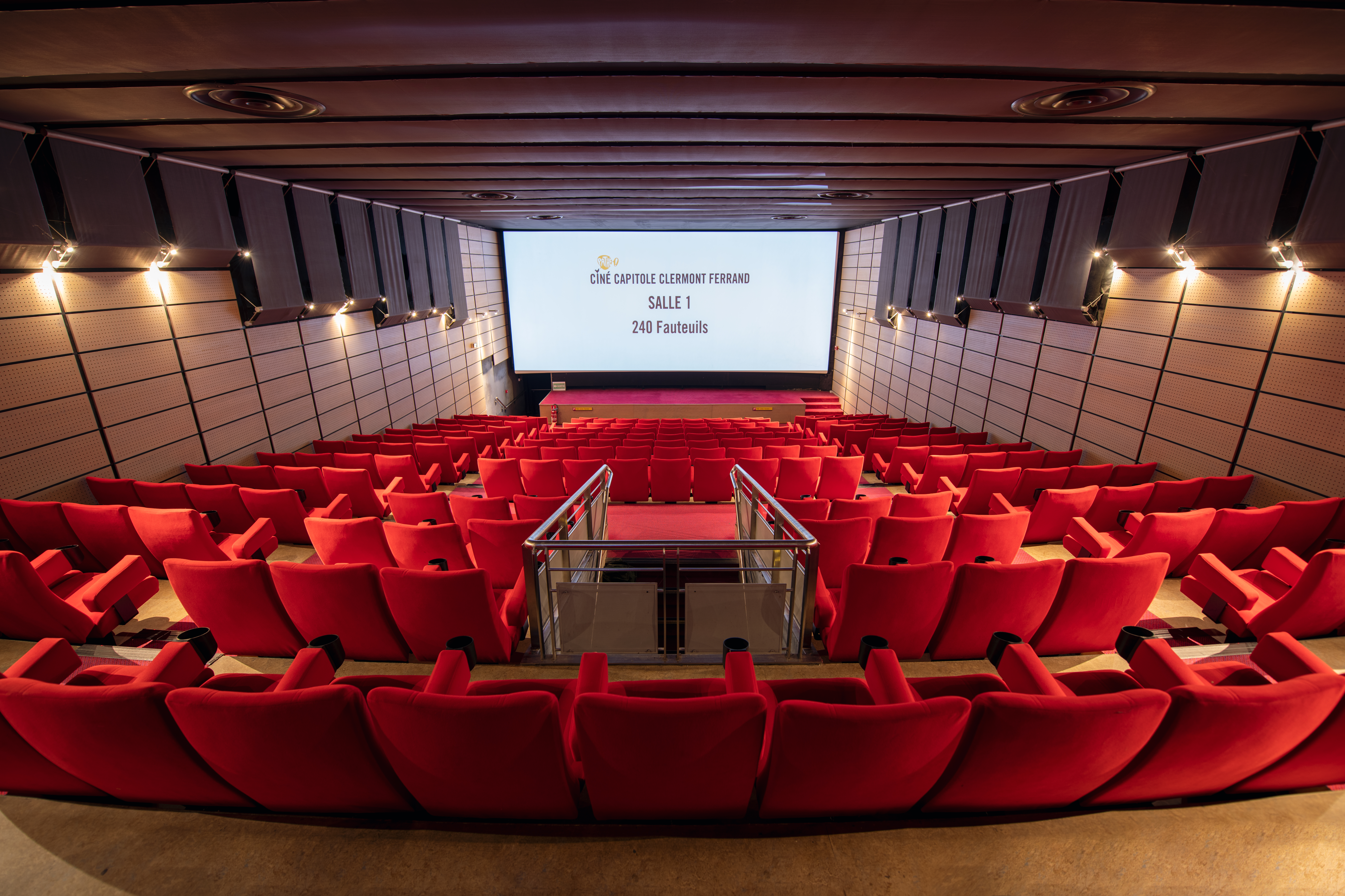 Vue depuis l’arrière de la salle 1 du cinéma Pathé Capitole Clermont Ferrand avec rangées de fauteuils en velours rouges orientés vers l’écran.